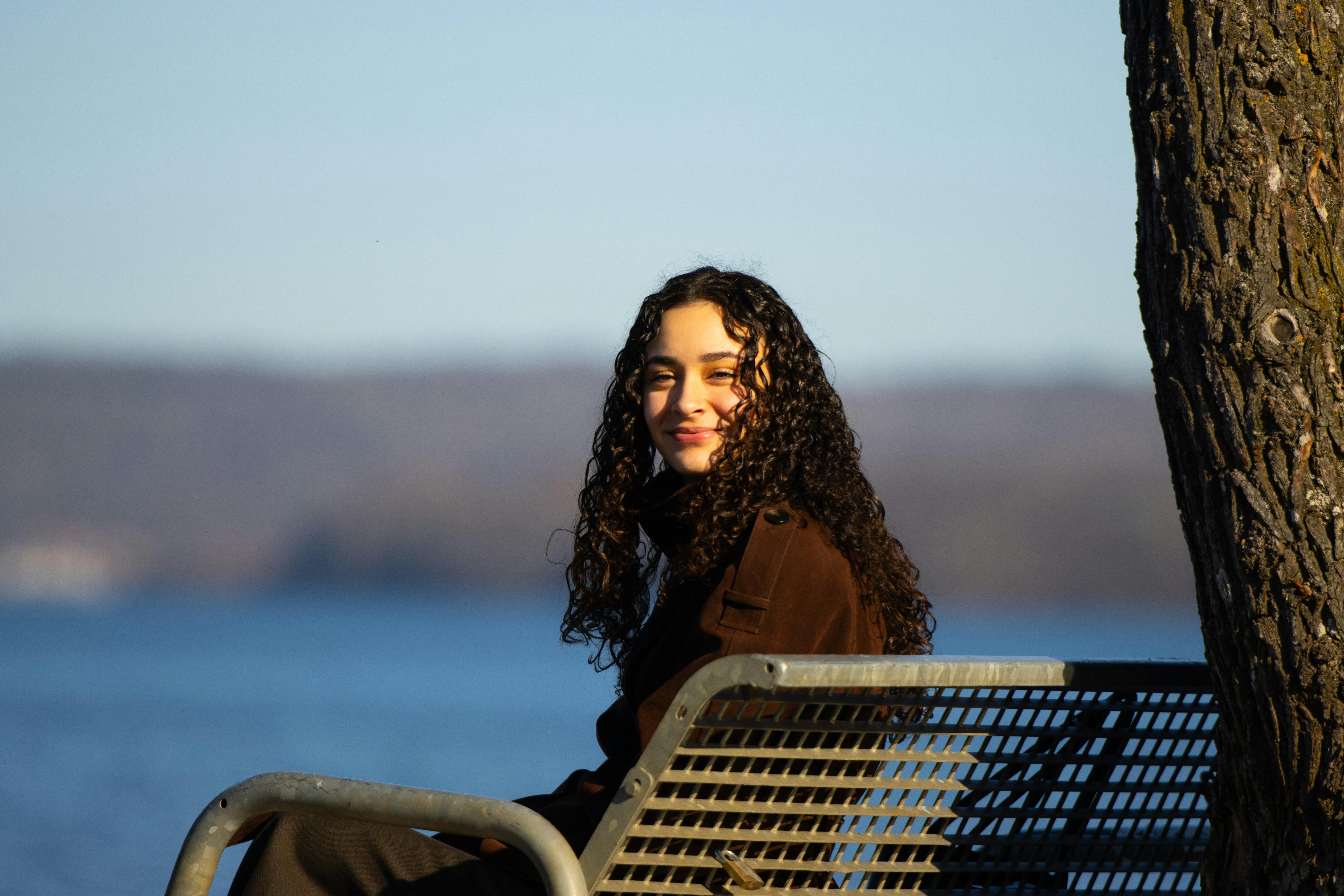 免費 一位女士坐在瑞典湖邊的長椅上，享受著寧靜的陽光。 圖庫相片