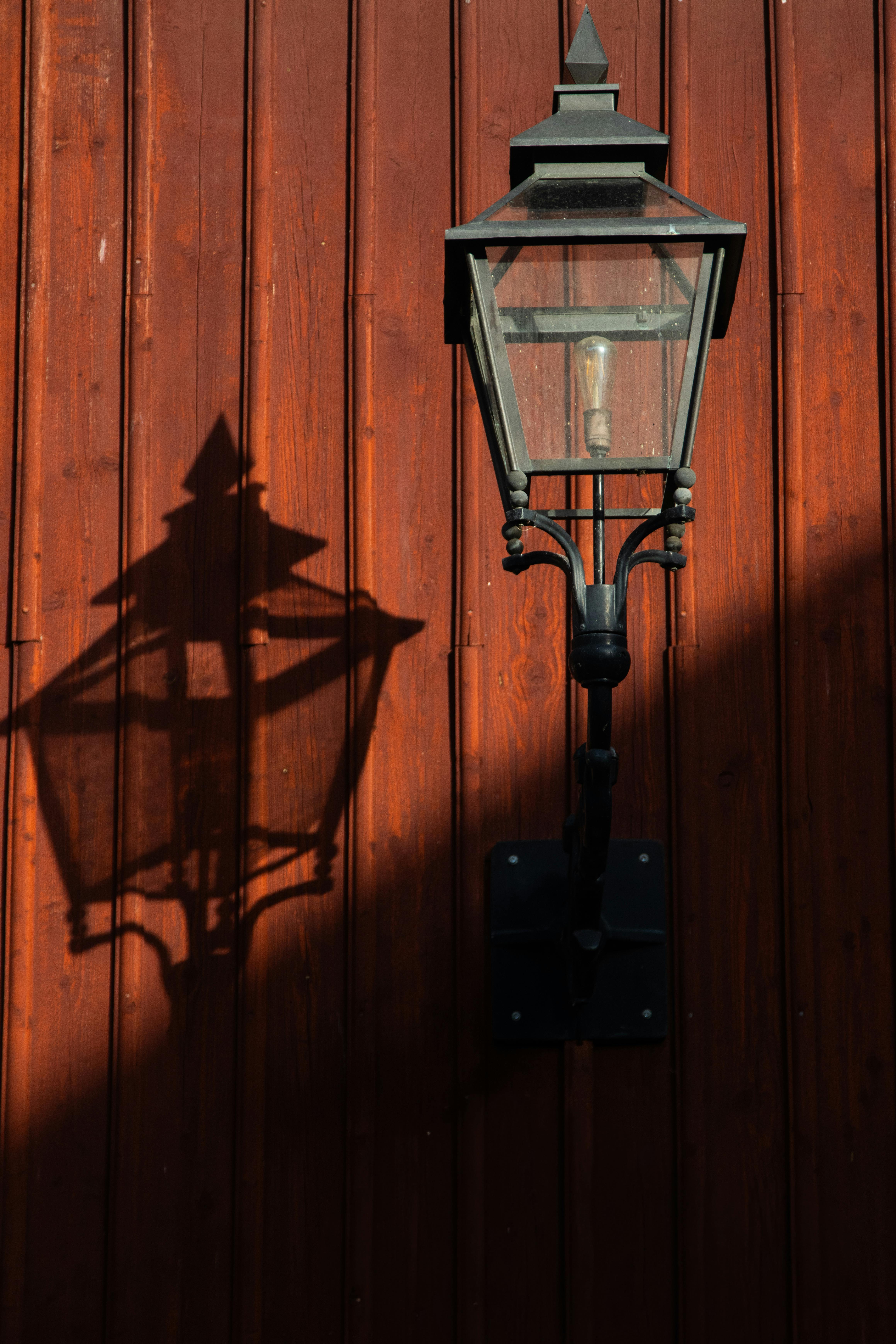 ฟรี โคมไฟโบราณที่มีเงาโดดเด่นตกกระทบผนังไม้สีแดงในเมืองยอนเชอปิง ประเทศสวีเดน คลังภาพถ่าย