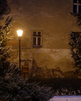 A warm street lamp illuminates a snowy urban wall with graffiti on a winter night.