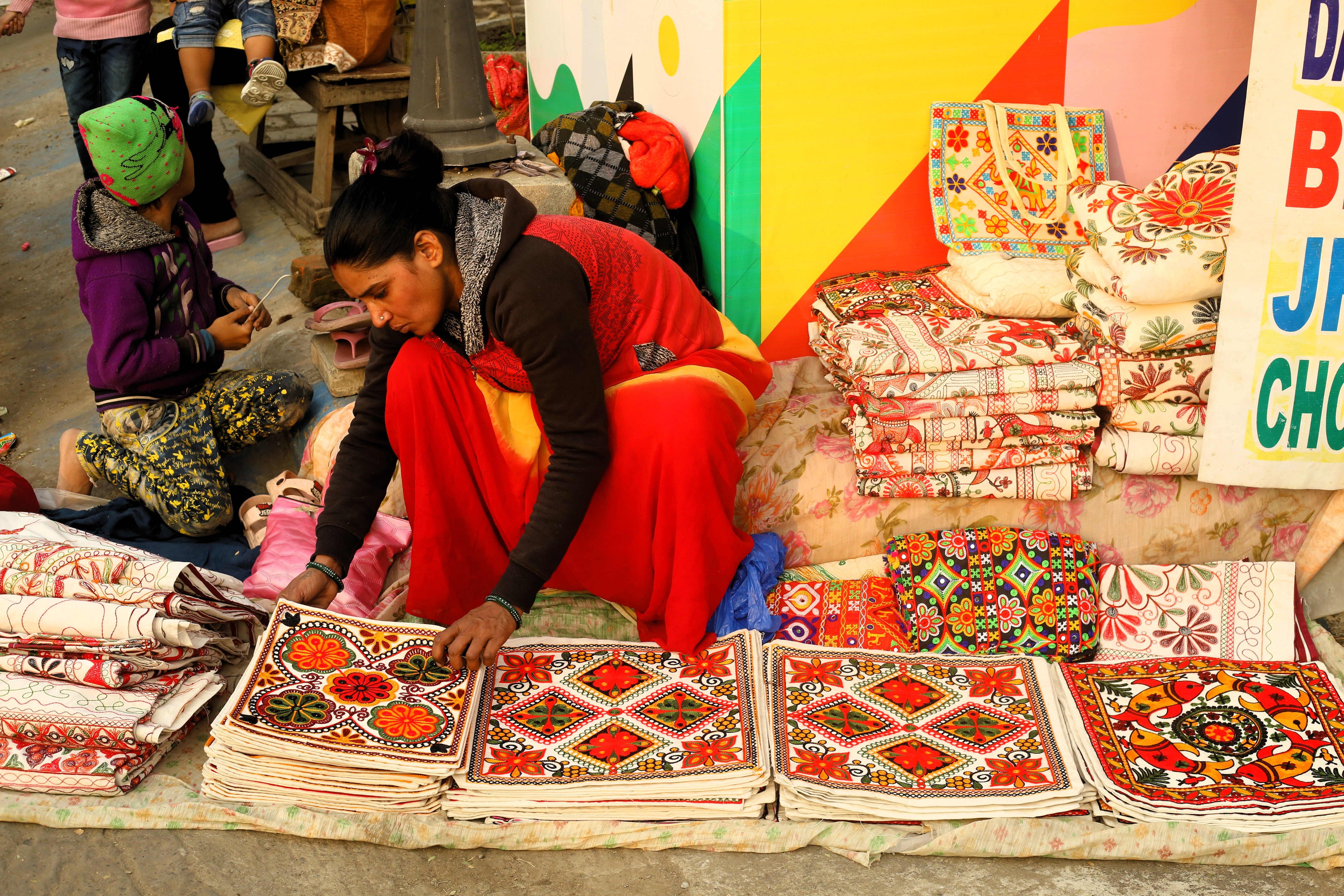 A woman arranges colorful fabrics at a lively outdoor market stall. — Maynard Longarm Quilting
