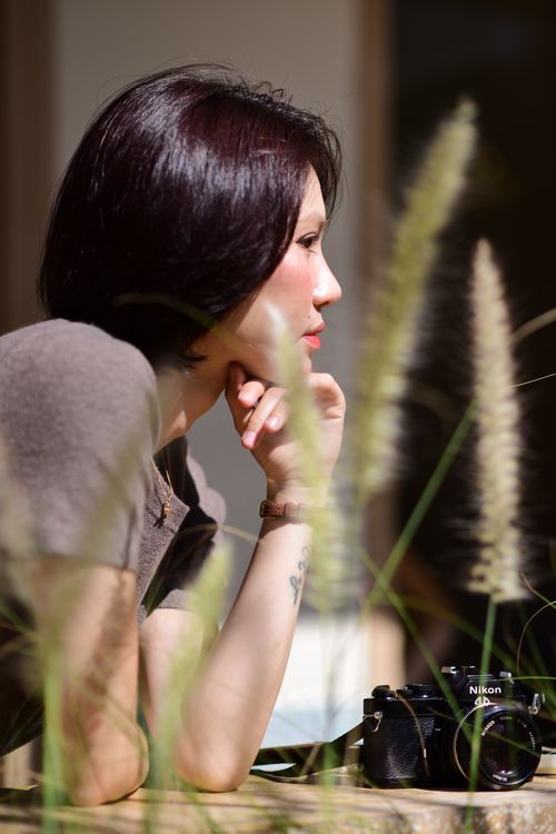 Free Side profile of a woman outdoors, her hand under chin, with a vintage camera beside her. Stock Photo