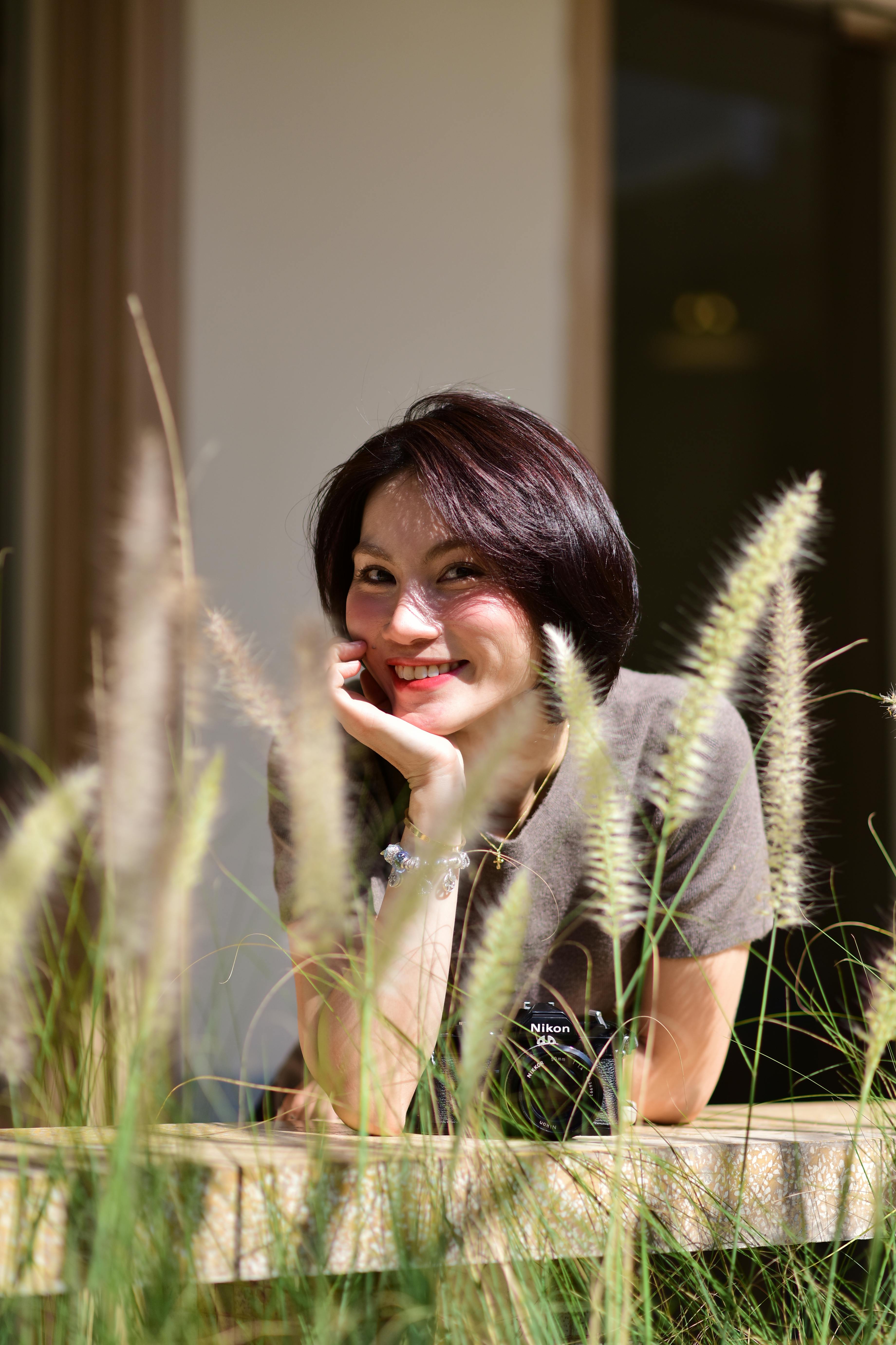 Безкоштовне Усміхнена жінка, спираючись на перила, оточена декоративною травою на вулиці. стокове фото