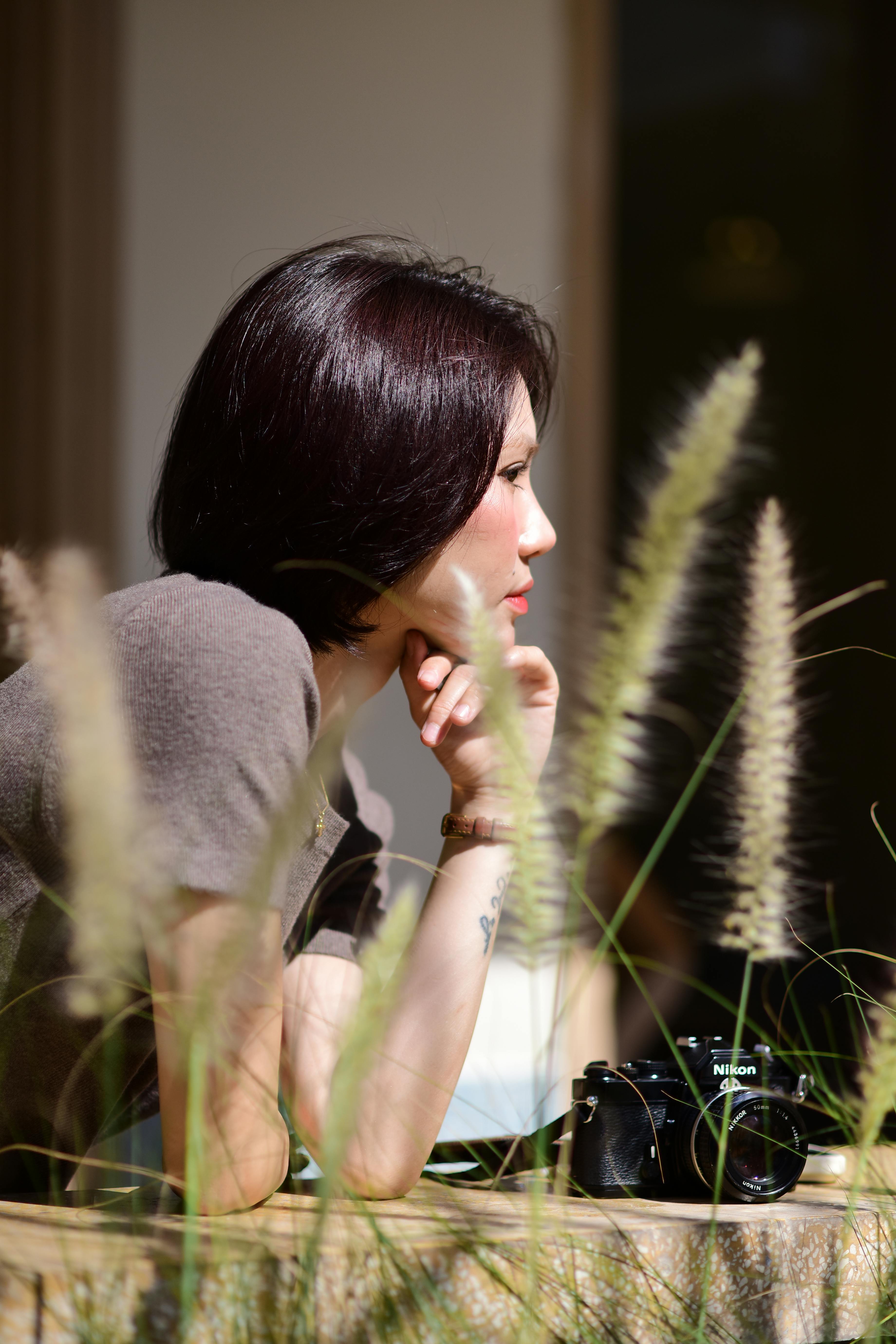 ฟรี หญิงสาวกำลังเพลิดเพลินกับวันแดดจ้ากลางแจ้ง โดยพิงราวระเบียงและมีกล้องวินเทจวางอยู่ข้างๆ คลังภาพถ่าย