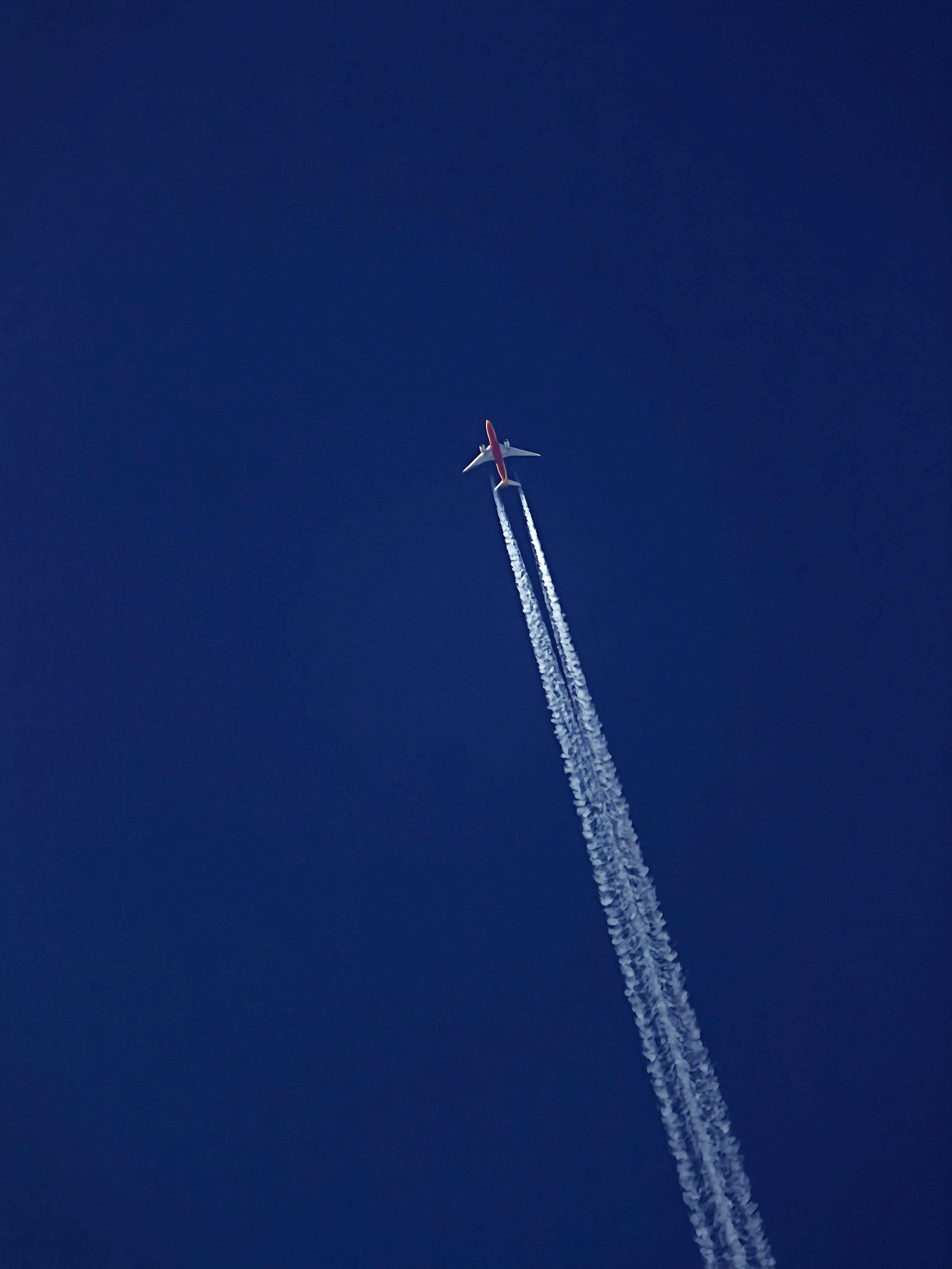 ingyenes Egy repülőgép sziluettje kondenzcsíkokkal a tiszta kék égen, alulról fényképezve. Stockfotó