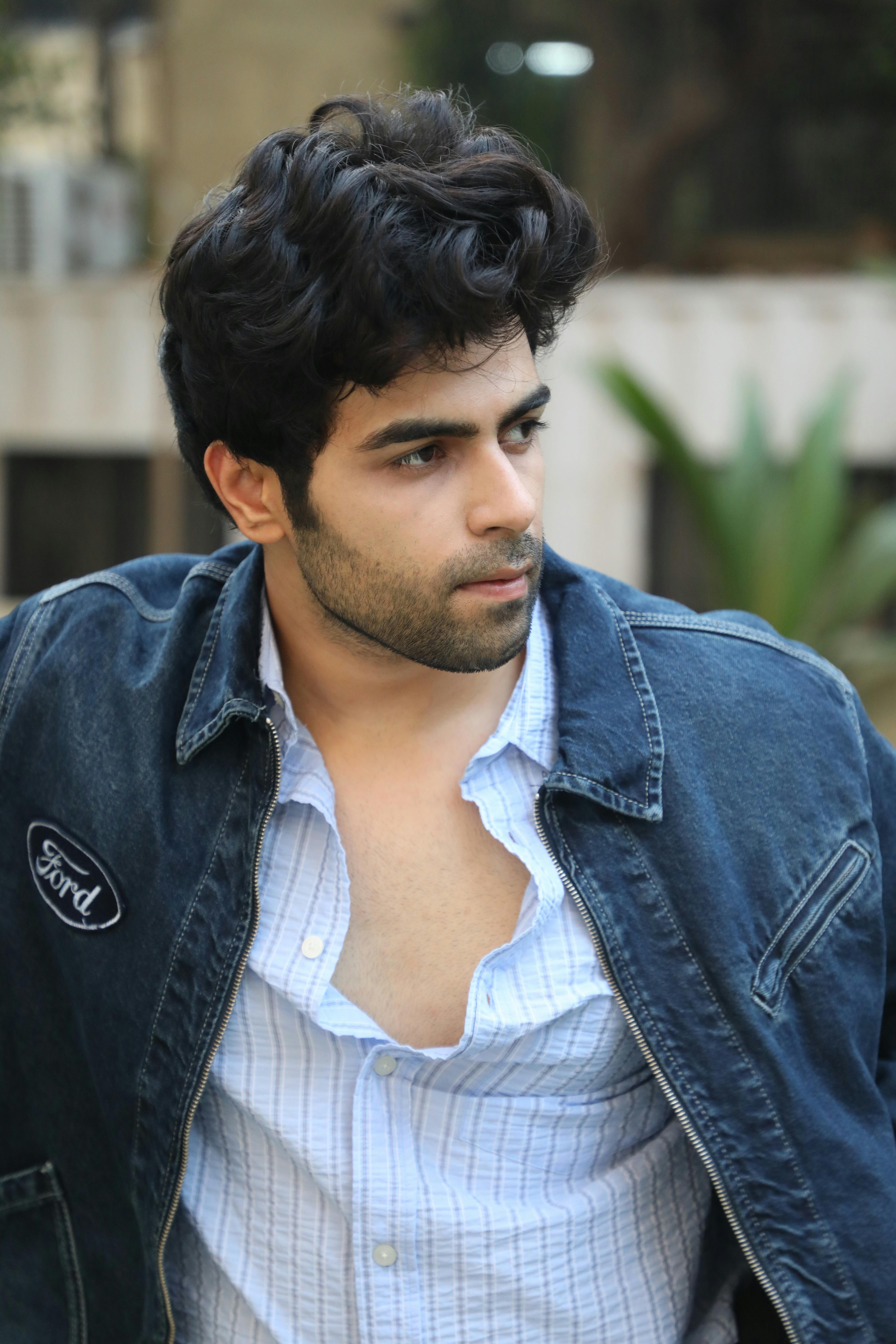 A stylish man in a denim jacket gazes thoughtfully outdoors.