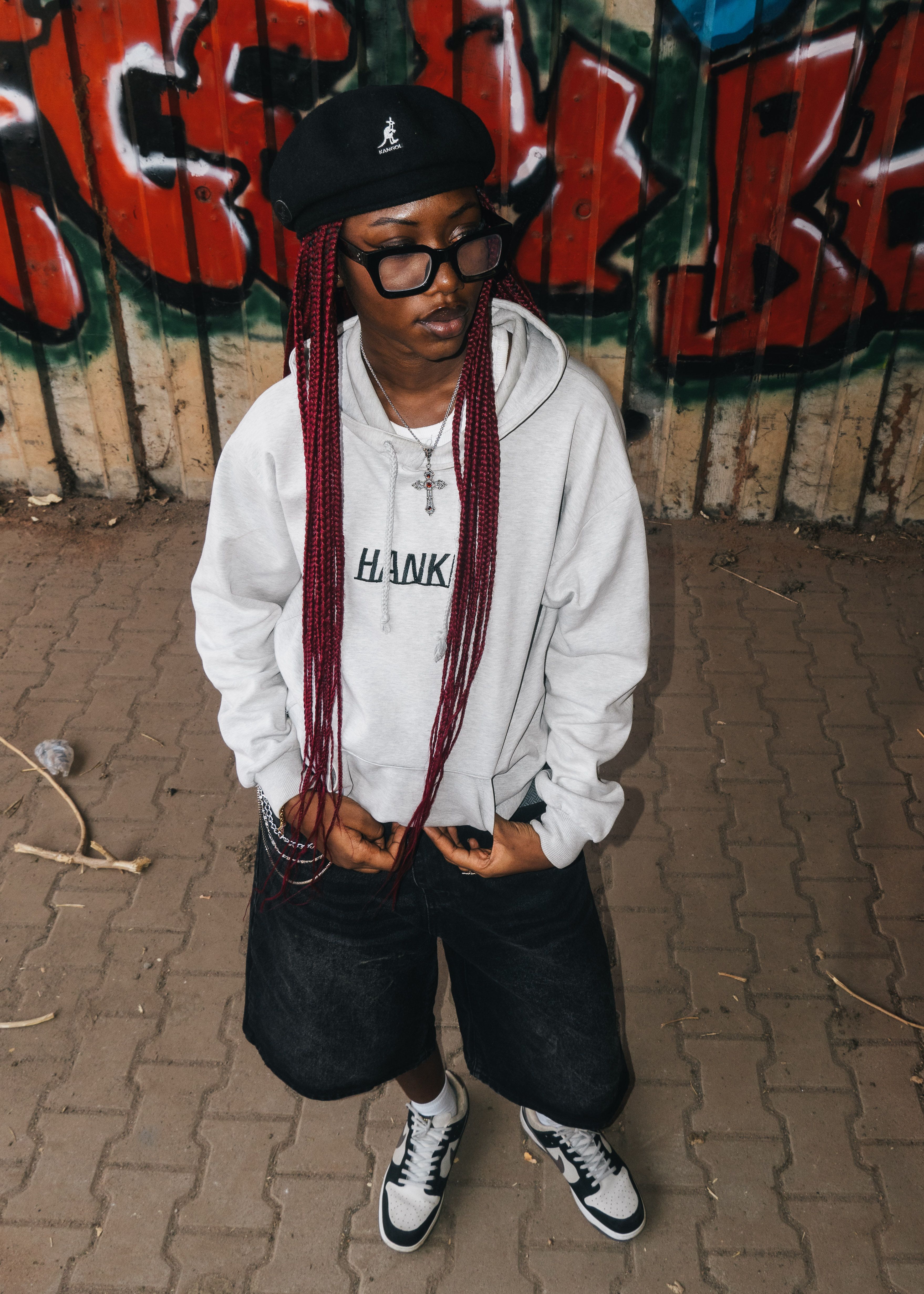 Fashionable young adult with red braids poses confidently against colorful graffiti in Abuja, Nigeria.