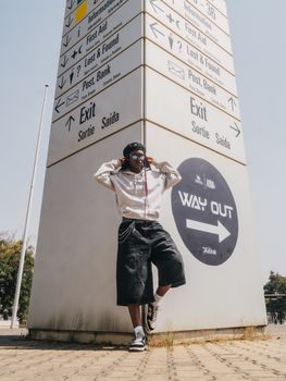 A trendy young adult posing by a directional sign in Abuja, Nigeria.