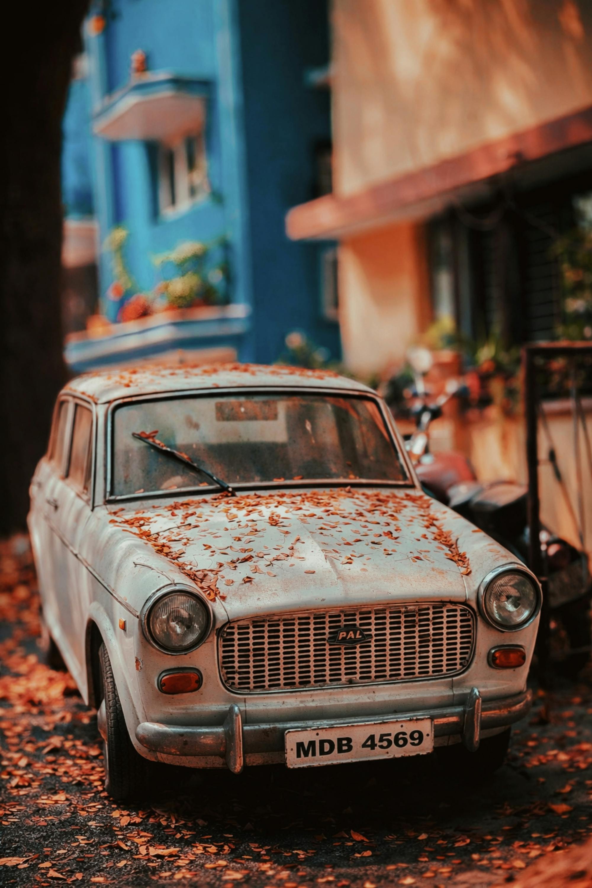 ingyenes Őszi levelekkel borított retró Fiat autó parkolt egy színes épületekkel teli városi utcán. Stockfotó