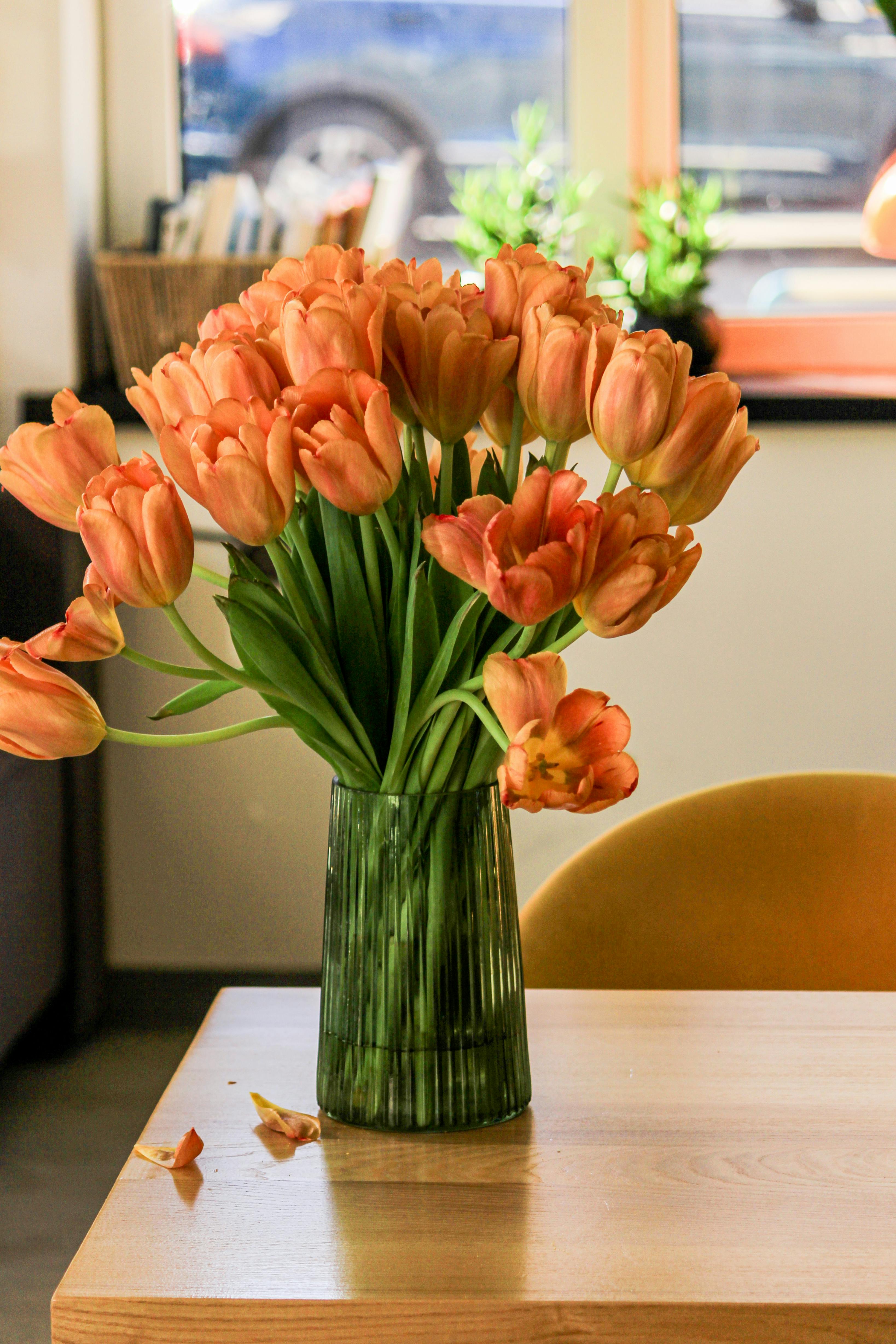 免费 阳光洒在桌子上，一束美丽的橙色郁金香插在绿色的花瓶里。 素材图片