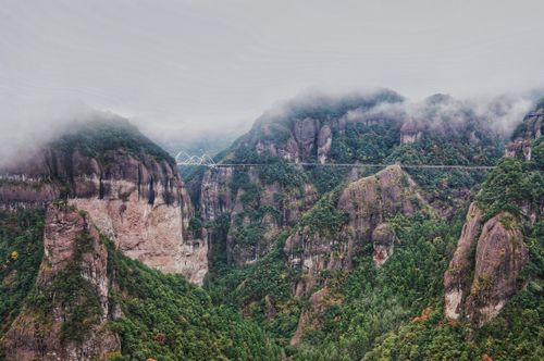 Free A scenic view of a misty mountain valley with a striking arch bridge blending with lush greenery. Stock Photo