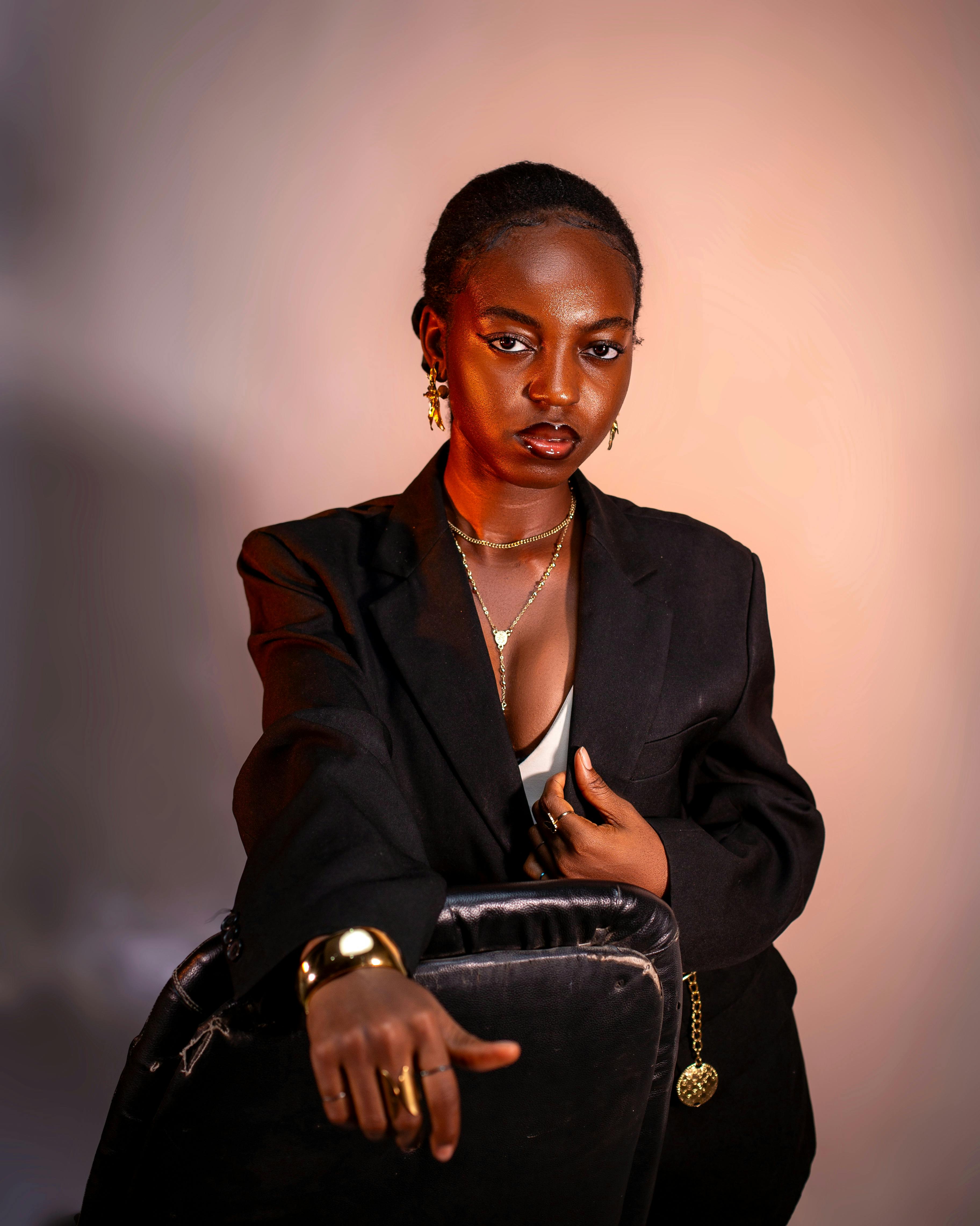 免費 一位身穿黑色西裝外套的時尚女士自信地擺出姿勢，手中拿著一張椅子，身上戴著金色首飾。 圖庫相片