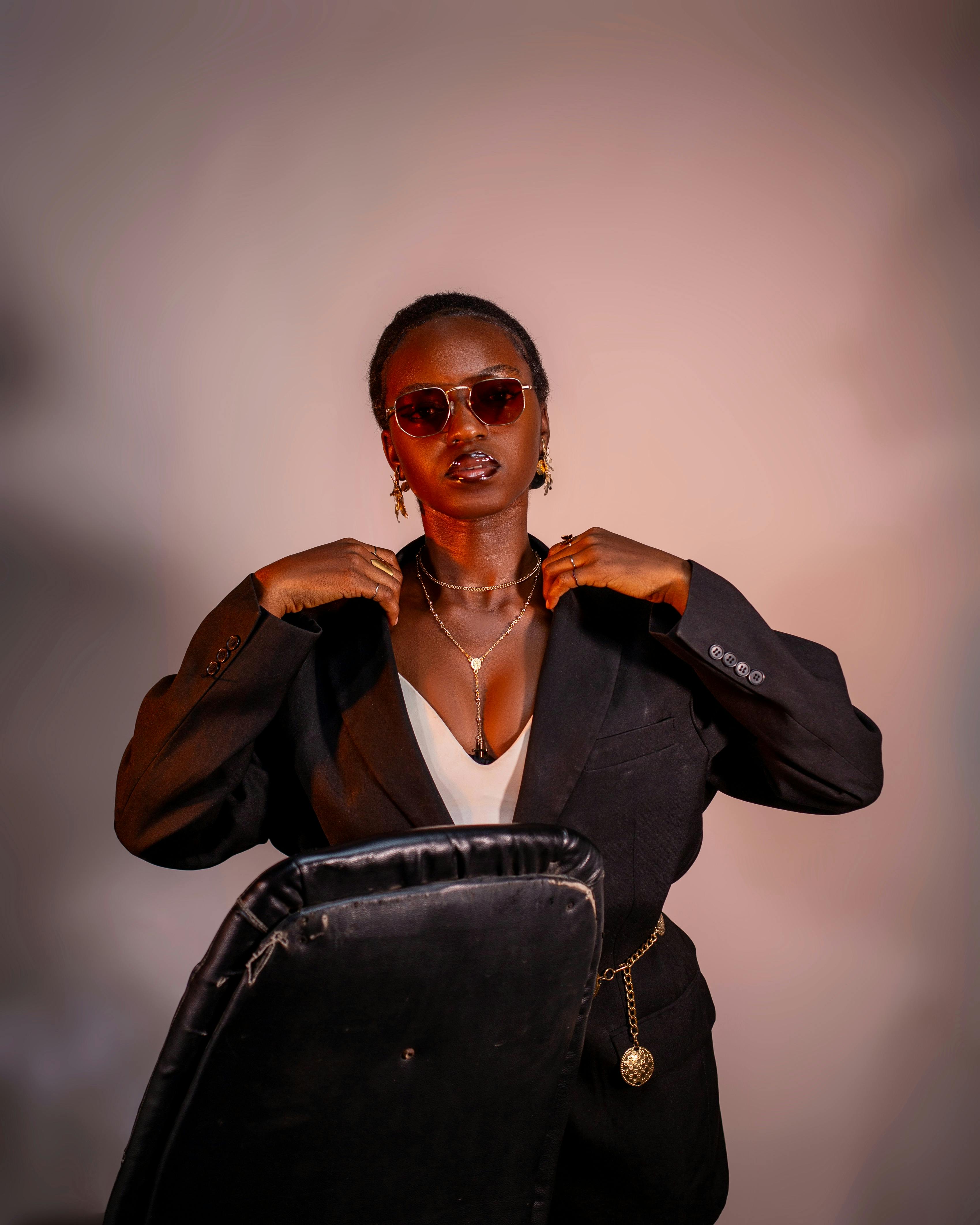 Безкоштовне Шикарна африканська жінка в сонцезахисних окулярах і чорному костюмі позує в приміщенні з елегантними ювелірними виробами. стокове фото