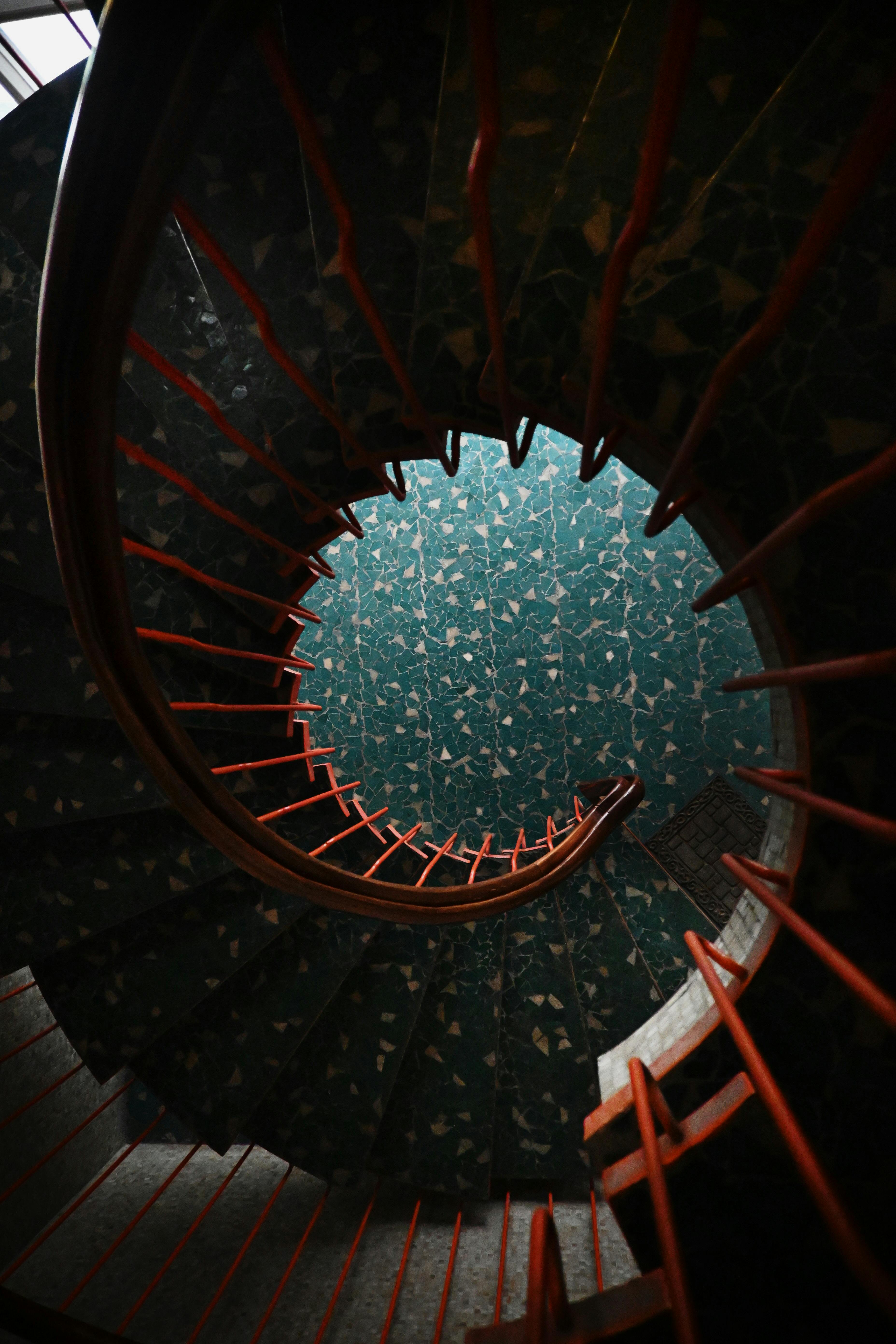 Безкоштовне Захопливі гвинтові сходи з червоними поручнями, що демонструють візерунчасту бірюзову підлогу, розташовані всередині. стокове фото