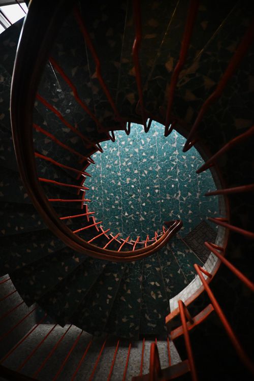 Free A mesmerizing spiral staircase with red railings showcasing a patterned teal floor, located indoors. Stock Photo