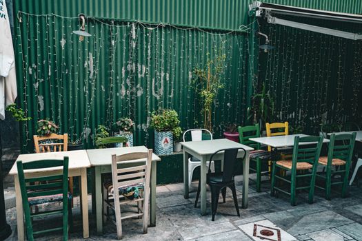Cozy outdoor café with eclectic chairs and ambient lights on a rustic green backdrop.