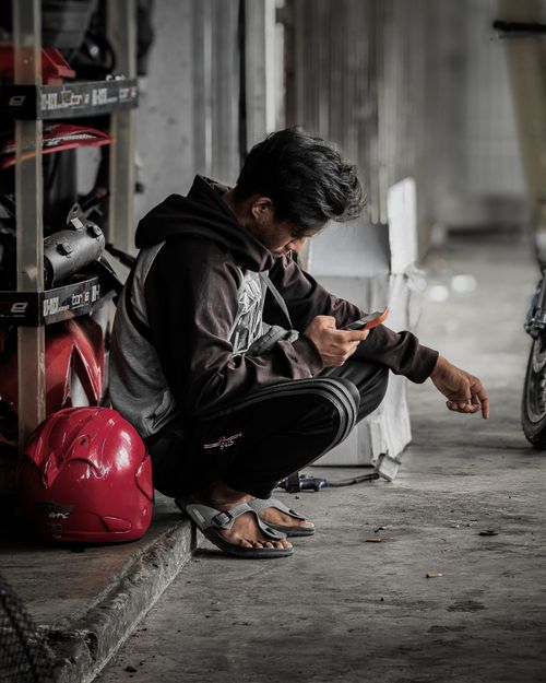 Free Man in casual wear sitting in a garage looking at his smartphone, Malaysia. Stock Photo