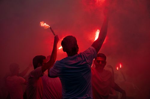 Free Vibrant crowd celebrating with red flares emitting smoke, creating a dynamic and festive atmosphere. Stock Photo
