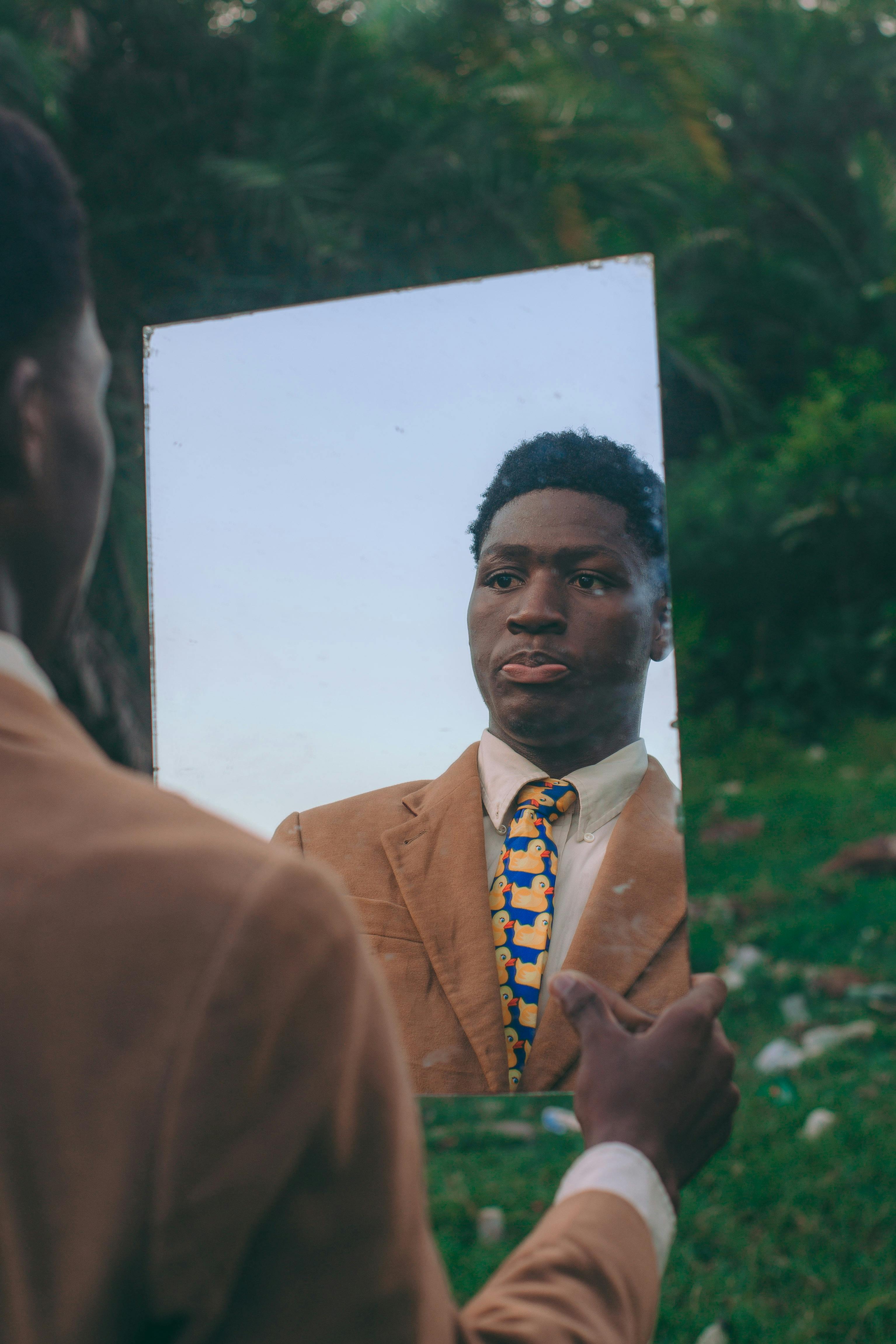 Zadarmo Muž v obleku drží zrkadlo v ruke, ktoré sa odráža v záhradnom prostredí v Akkre v Ghane. Fotka z fotobanky