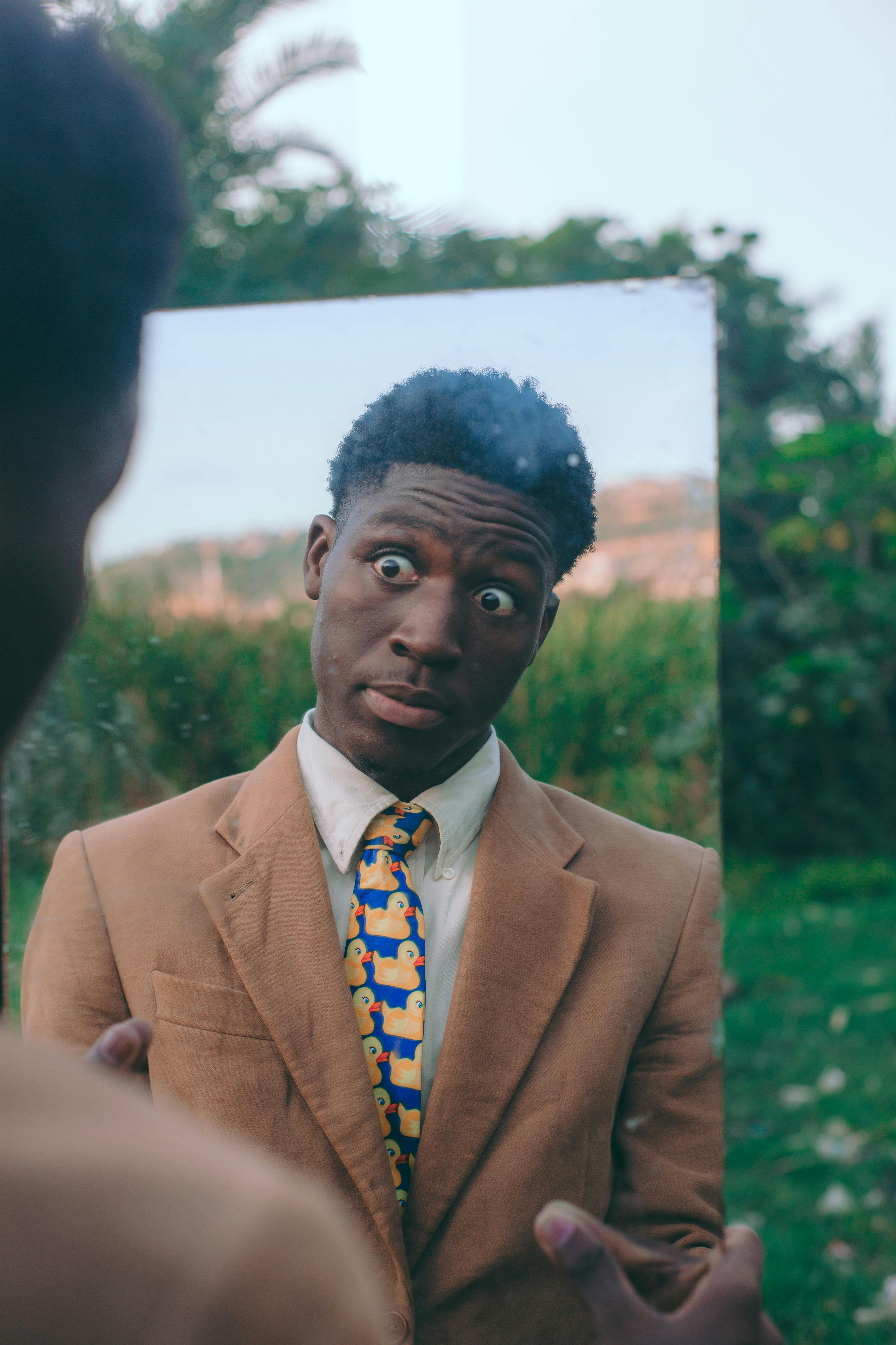 Безкоштовне Молодий чоловік робить жартівливий вираз обличчя, дивлячись у дзеркало на вулиці. Знято в Аккрі, Гана. стокове фото