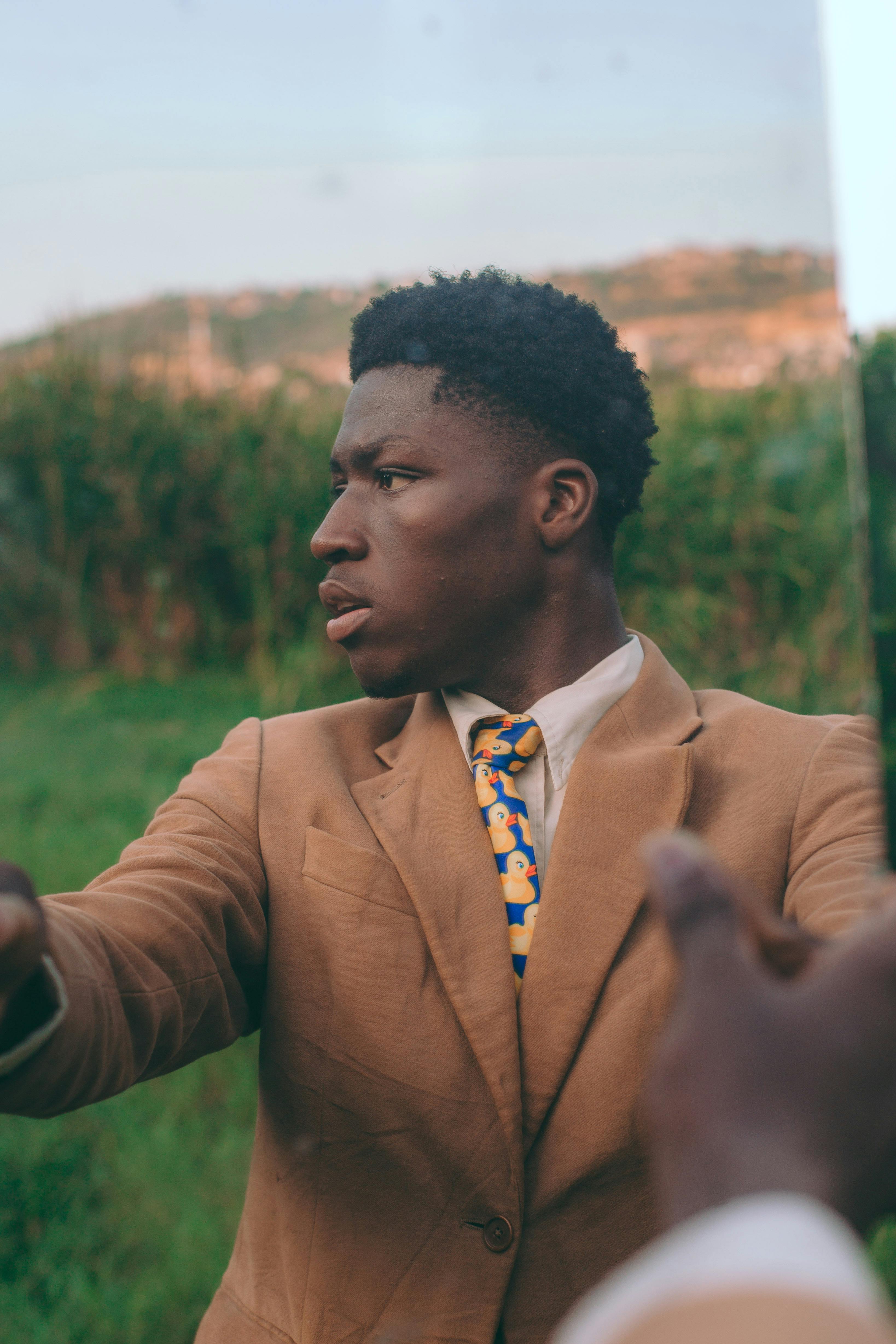 Безкоштовне Молодий чоловік у коричневому костюмі задумливо виглядає на свіжому повітрі в Аккрі, Гана. стокове фото