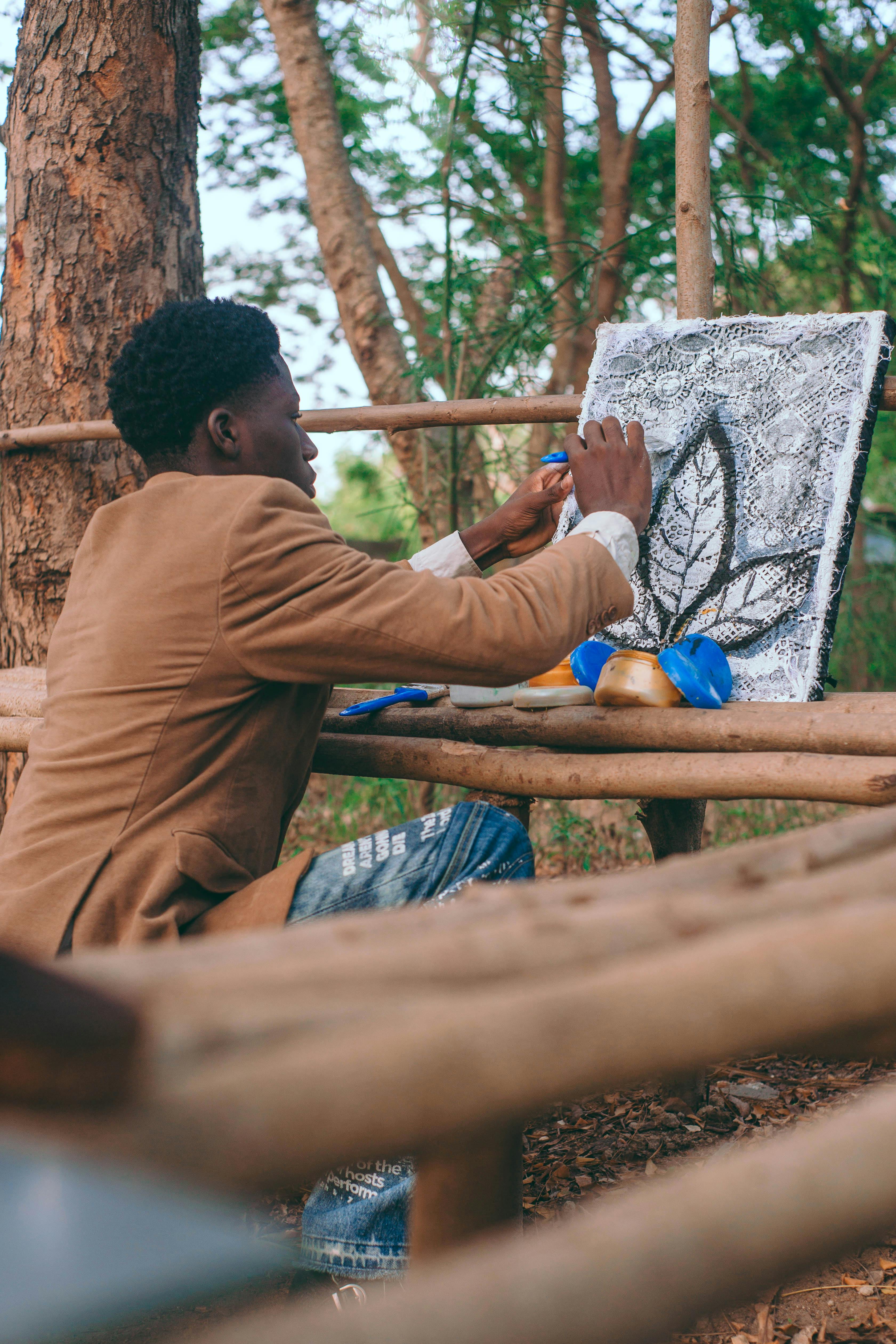 免費 在阿克拉寧靜的戶外環境中，一名非洲男子正在畫布上繪製樹葉圖案。 圖庫相片