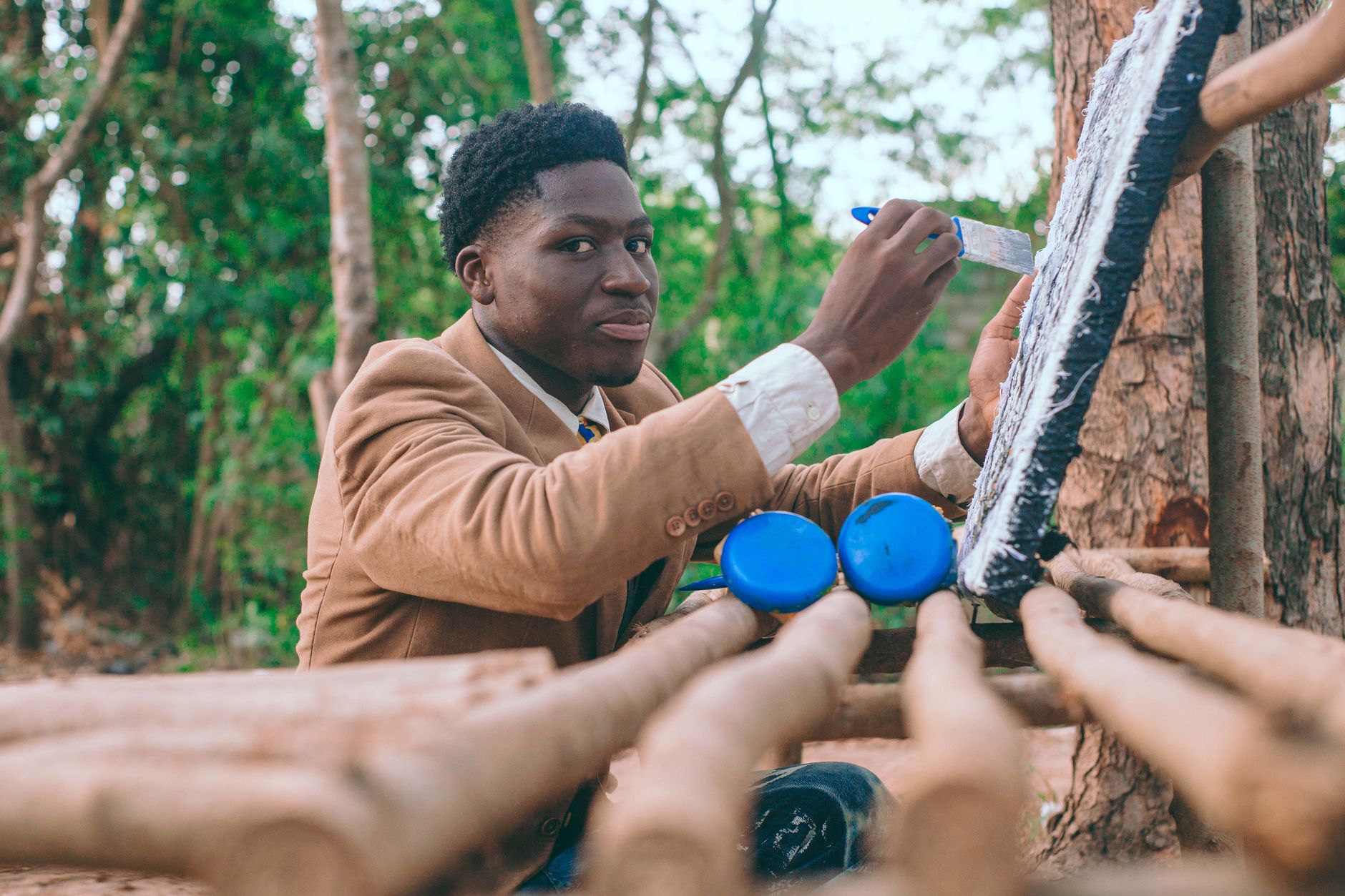 A young African artist painting on a canvas in an outdoor setting in Accra, Ghana.
