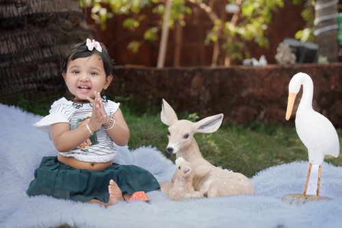 Free A cute toddler clapping joyfully outdoors among statues of a deer and a crane. Stock Photo