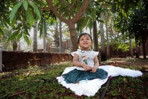 Free A cheerful child sitting under a tree, surrounded by lush greenery, enjoying a sunny day. Stock Photo