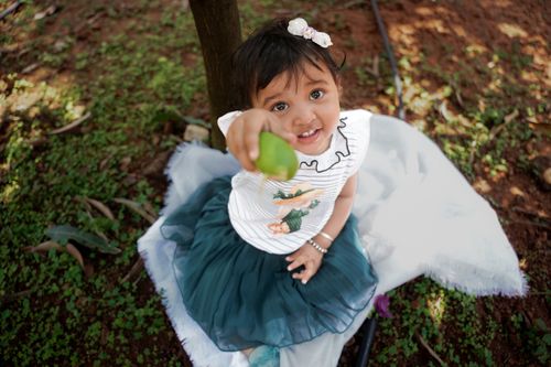 Free A cute toddler cheerfully holds a lime, enjoying a sunny day outdoors on a grassy field. Stock Photo
