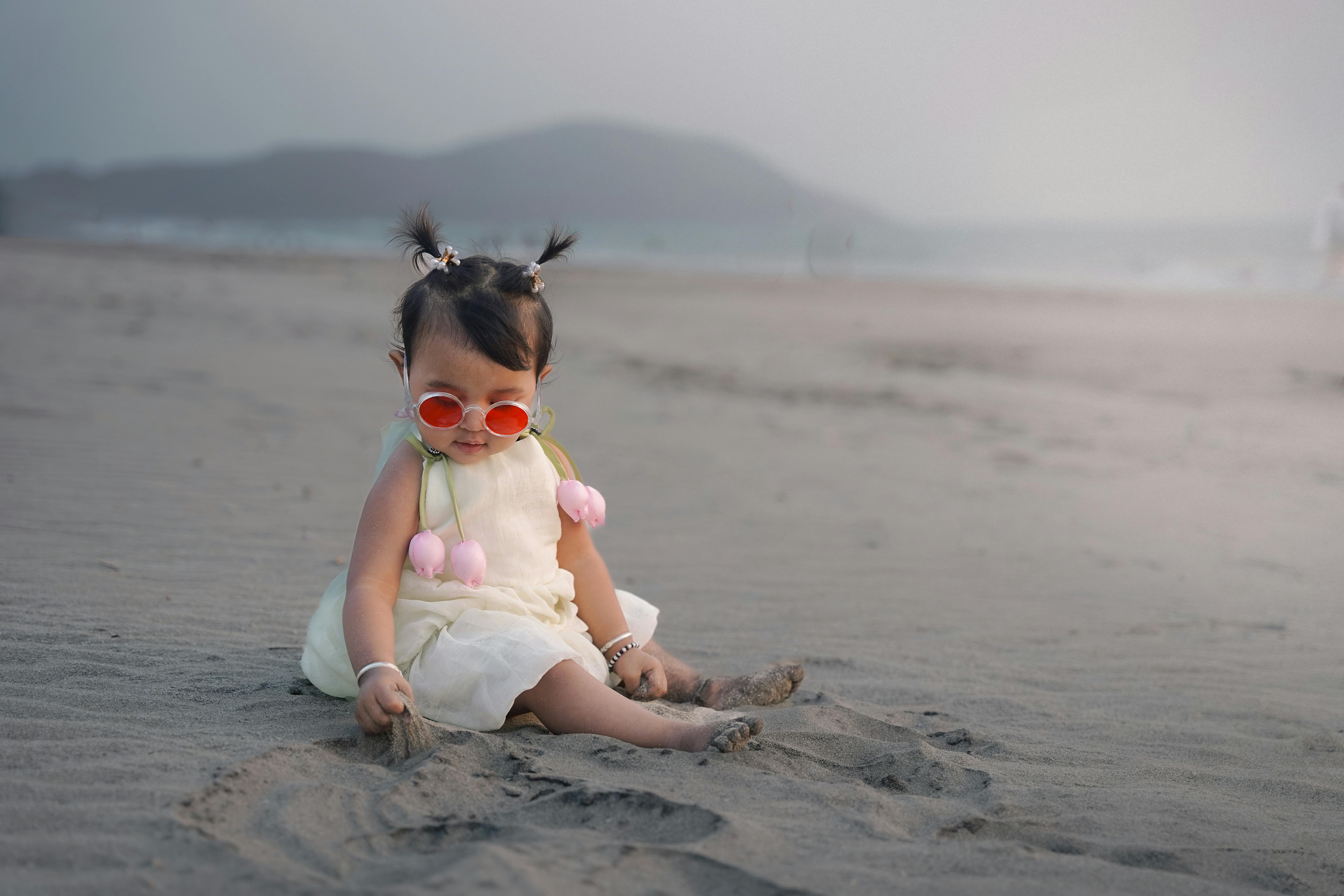 Zadarmo Roztomilé dievčatko so slnečnými okuliarmi si užíva hranie na piesočnatej pláži. Fotka z fotobanky