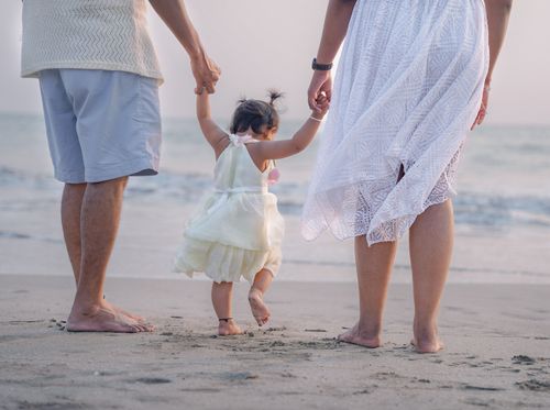 Free A family with a baby walks barefoot on the sandy beach during sunset, creating a beautiful, serene moment. Stock Photo