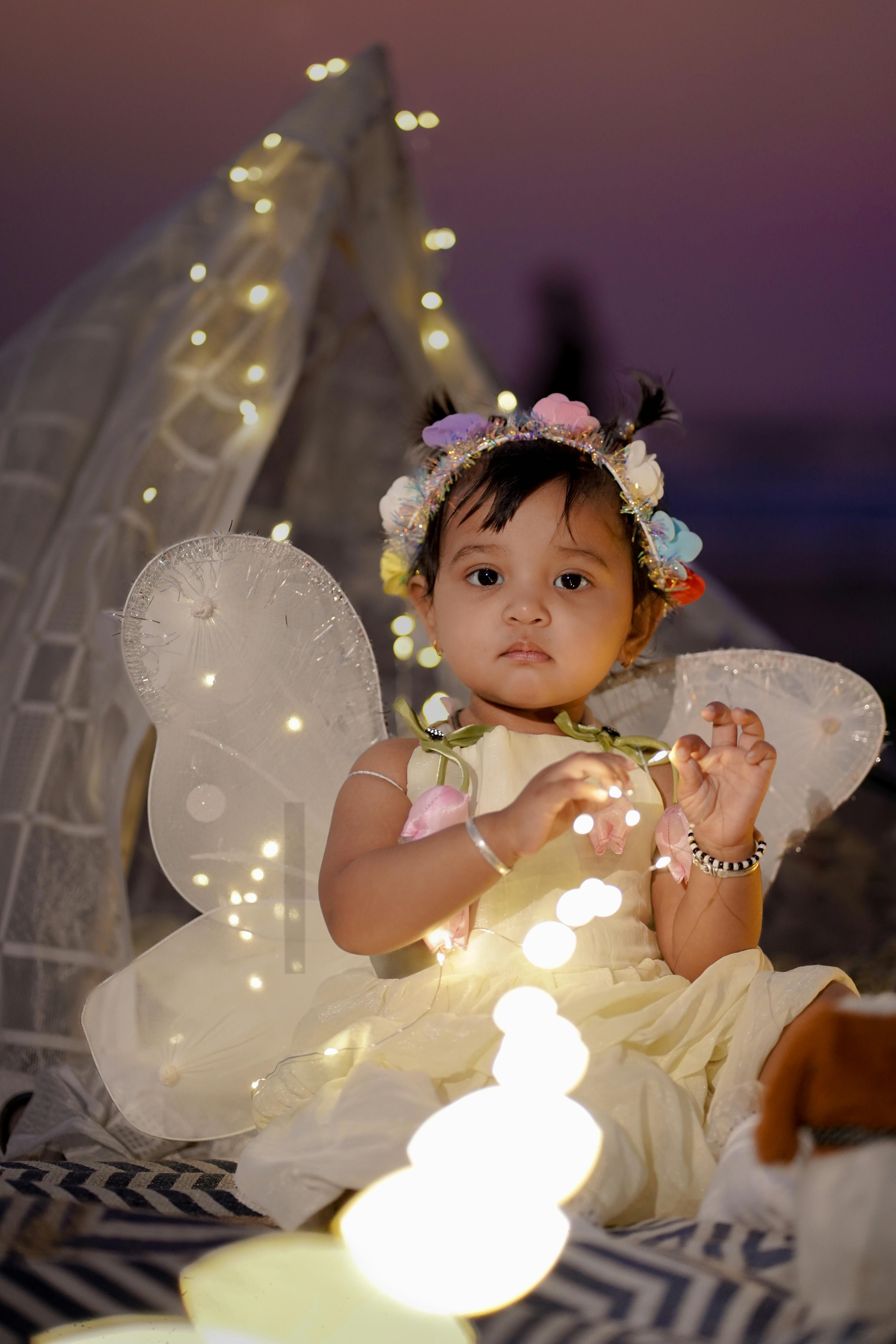 Безкоштовне Чарівна маленька дитина, одягнена в костюм феї, під час вечірнього заходу на свіжому повітрі, освітленого м'якими гірляндами. стокове фото