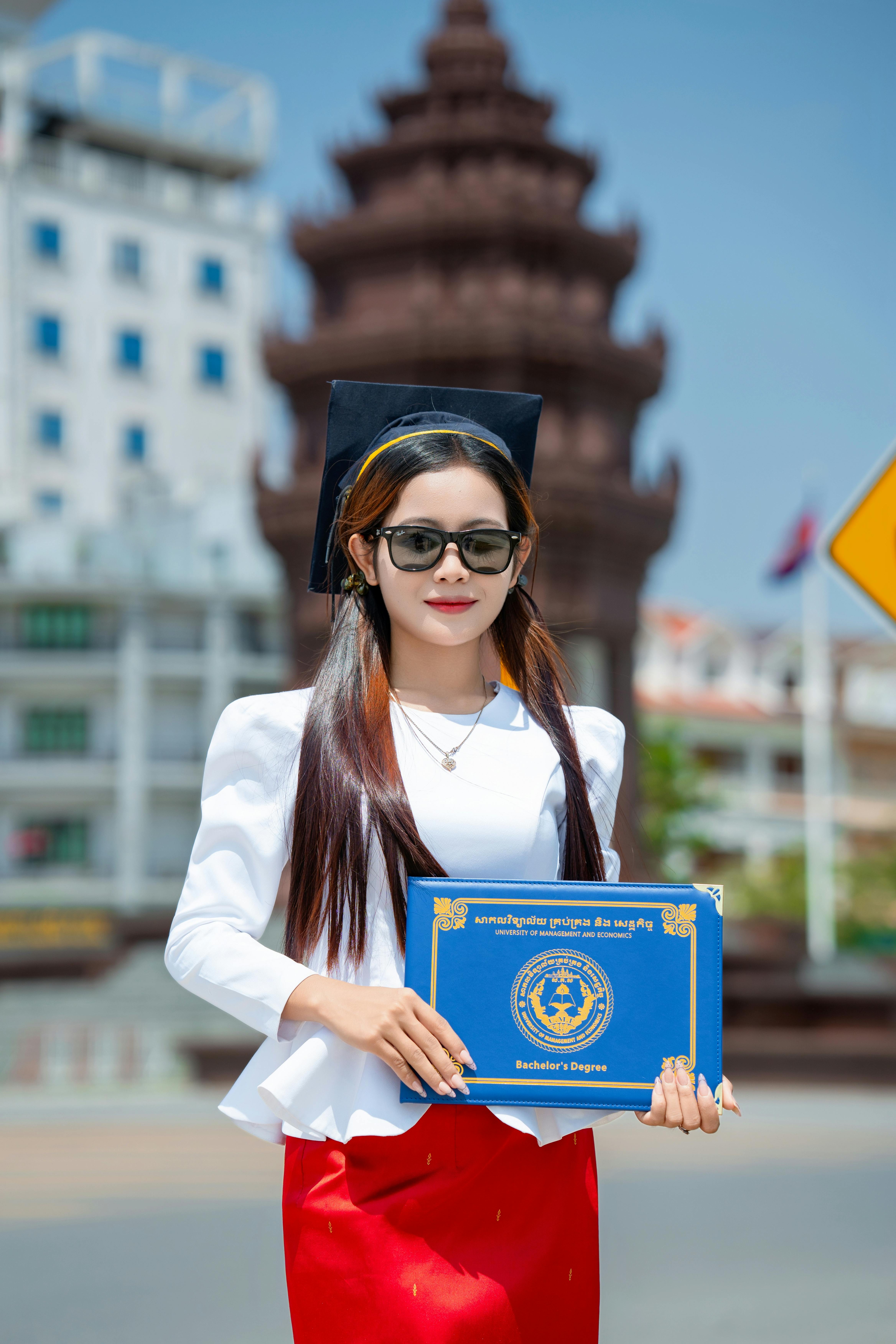 Zadarmo Mladý absolvent v čiapke a talári drží diplom vonku za slnečného dňa. Fotka z fotobanky