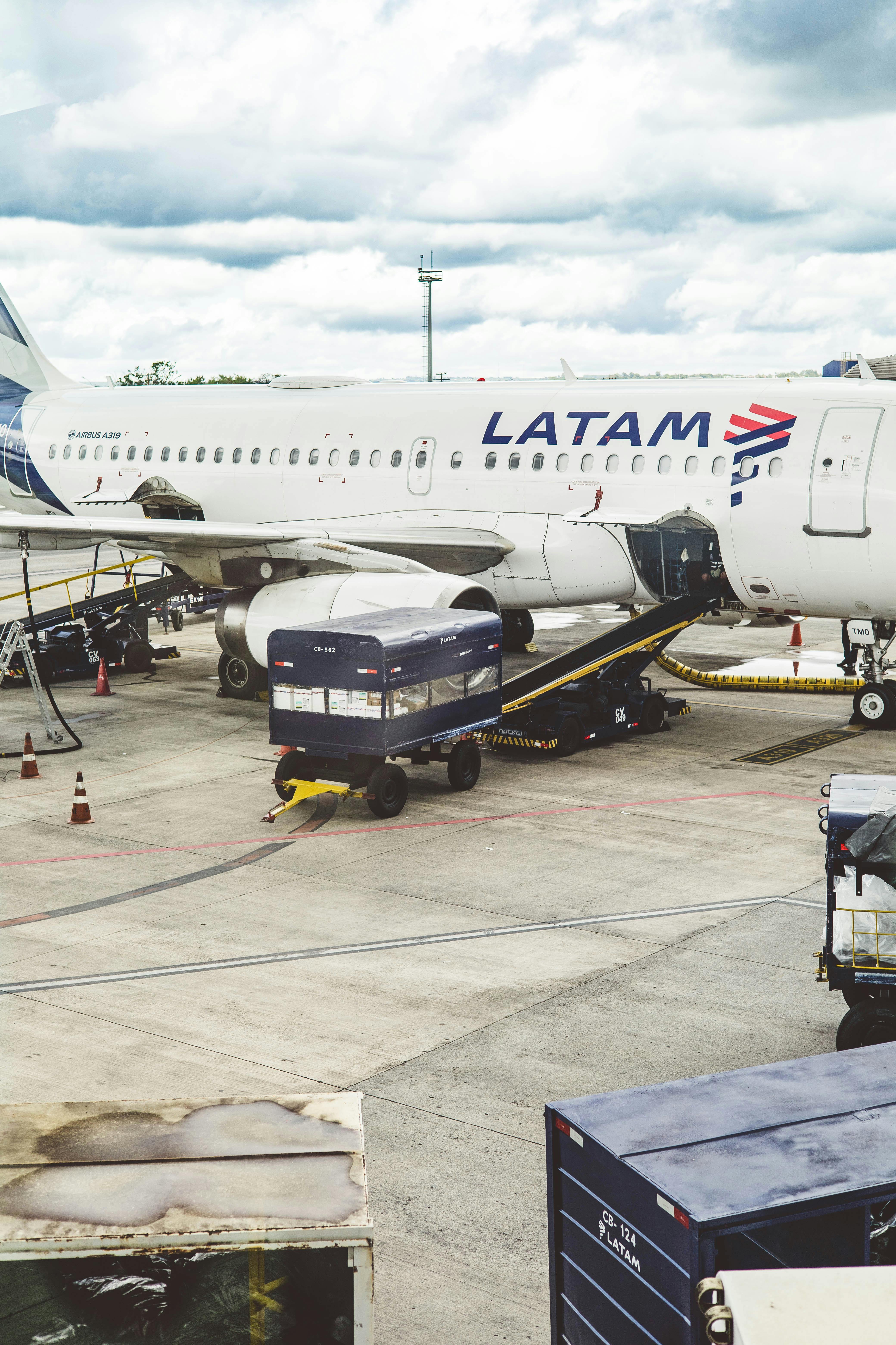 LATAM Airlines airplane being serviced at airport terminal with cloudy sky above.