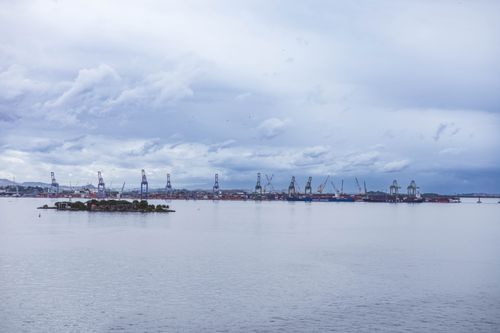 Free A tranquil ocean view with a distant industrial skyline under a cloudy sky, perfect for themes of industry and nature contrast. Stock Photo