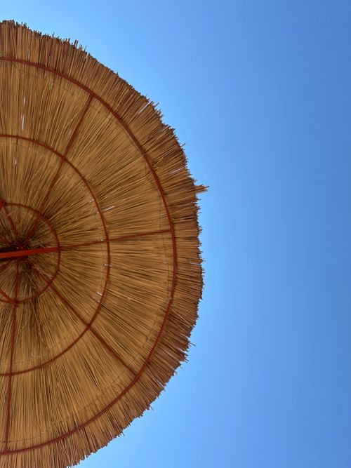 Free A straw beach umbrella set against a clear blue sky in Glyfada, Greece. Stock Photo