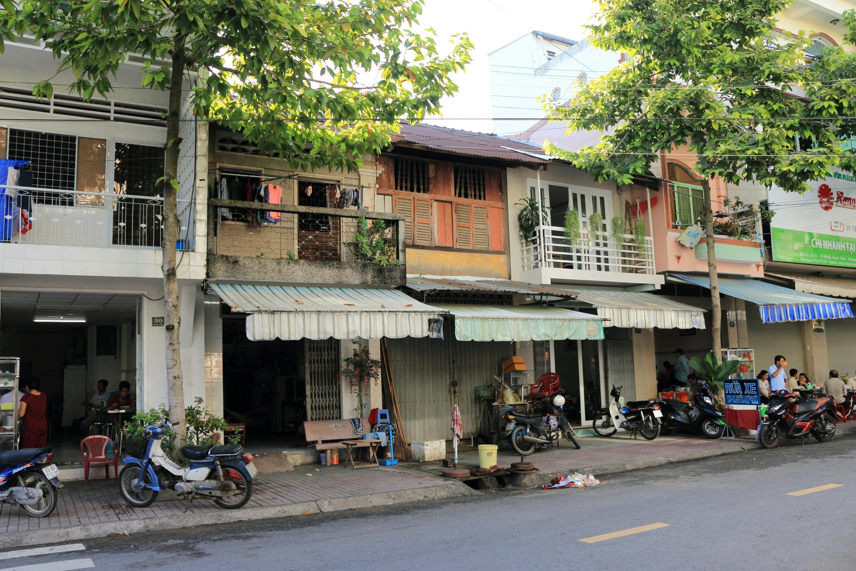 免費 越南古色古香的城市街道，有當地商店、摩托車和樹木。 圖庫相片