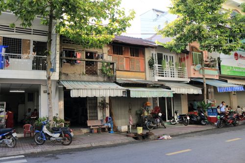 Free Quaint city street in Vietnam featuring local shops, motorbikes, and trees. Stock Photo