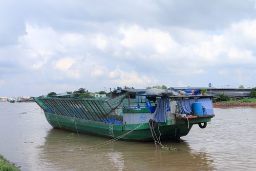 Free A traditional boat docked on a river in Vietnam under a cloudy sky. Stock Photo