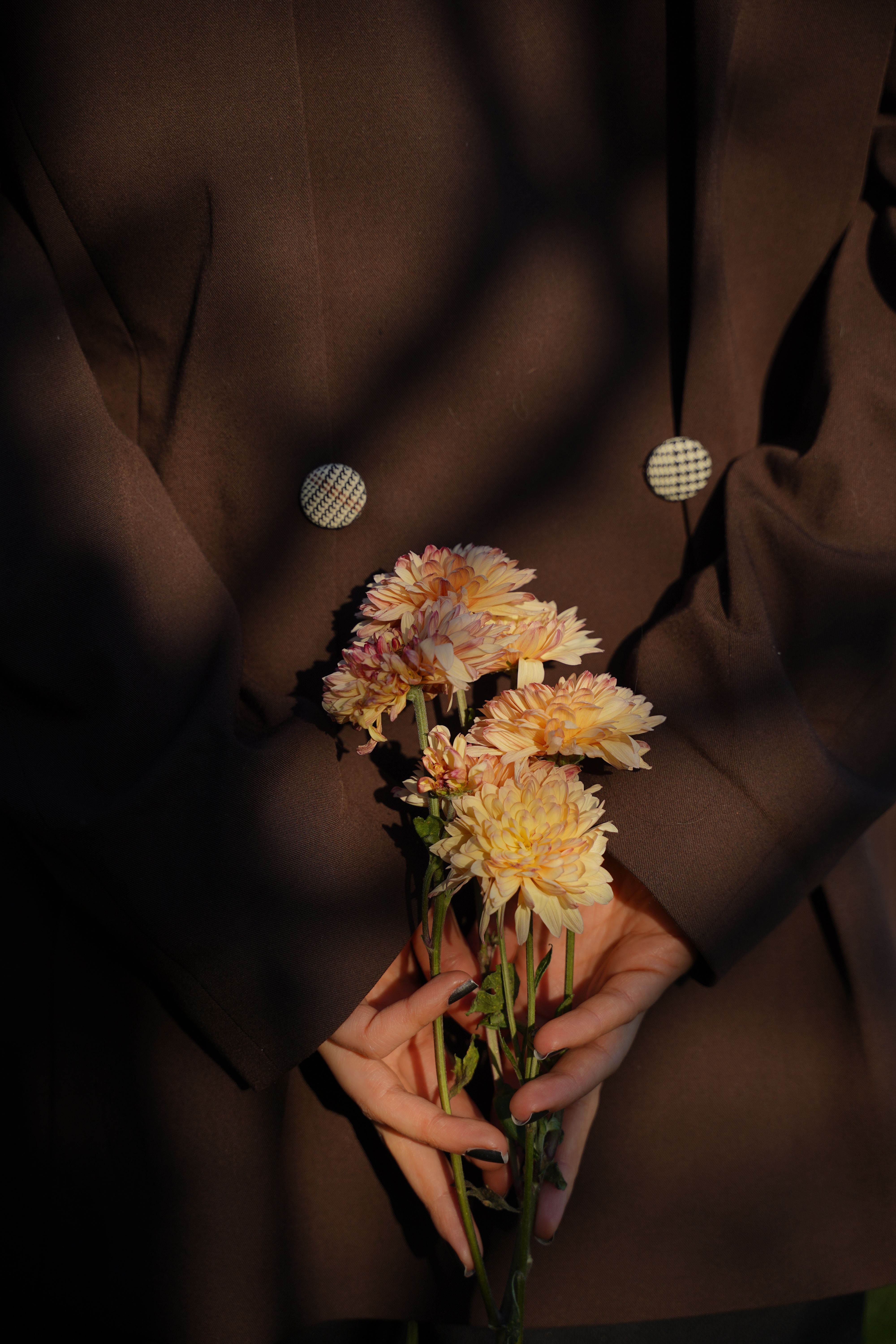 Close-up of hands holding flowers against a brown jacket, casting artistic shadows.
