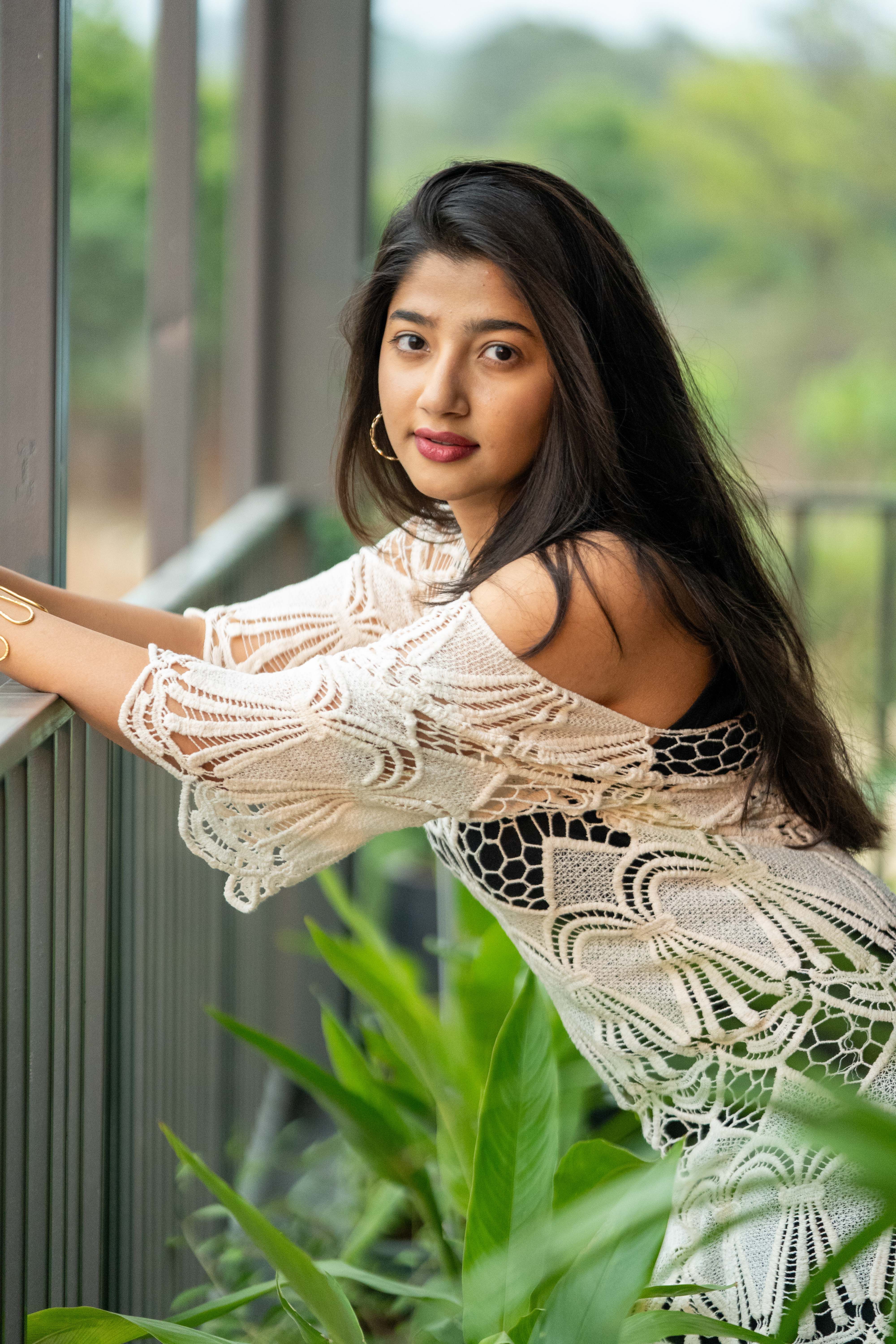 A stylish woman in a lace dress posing outdoors with greenery and soft natural light, conveying elegance.