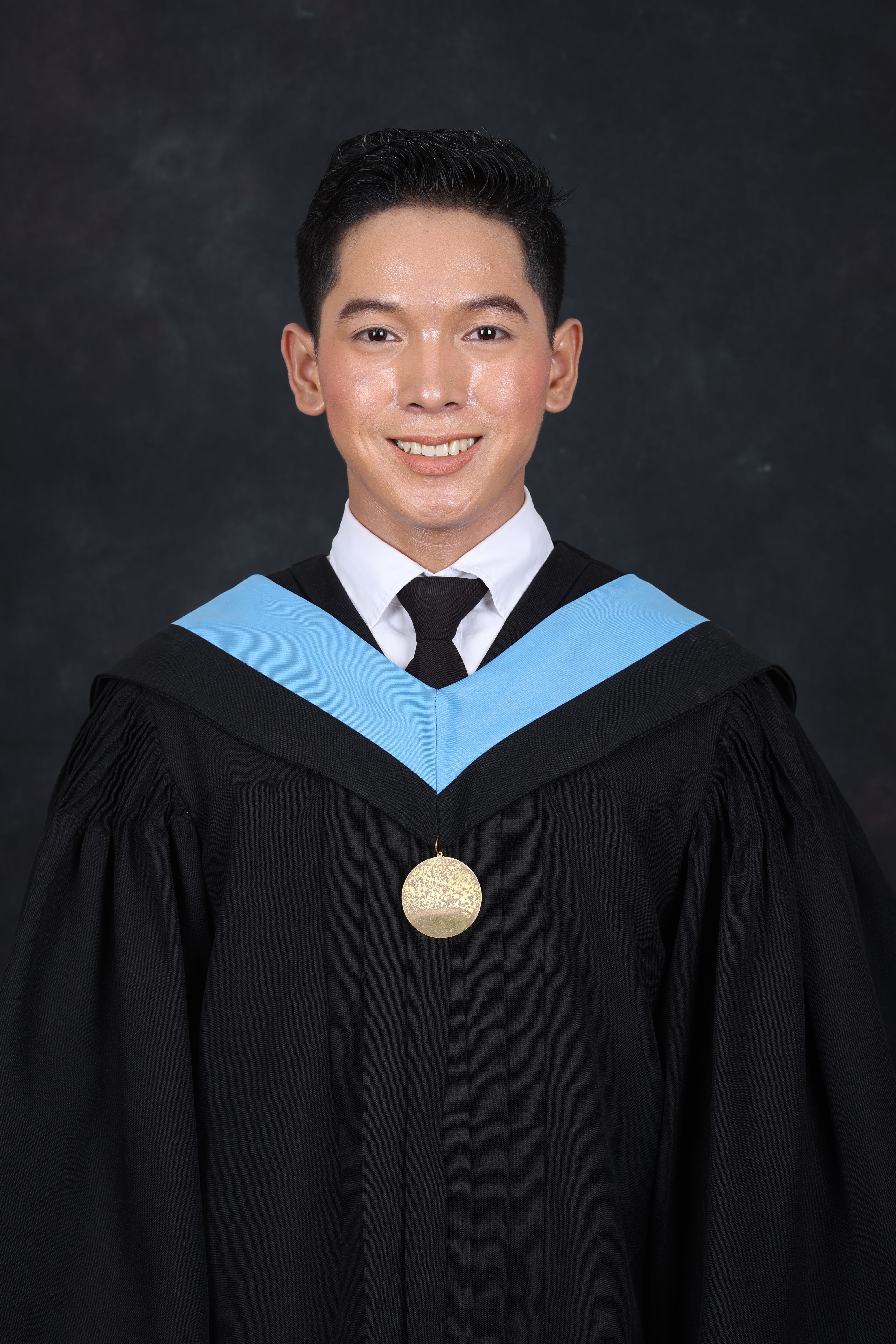 Formal graduation portrait of a smiling adult in cap and gown with a medal.