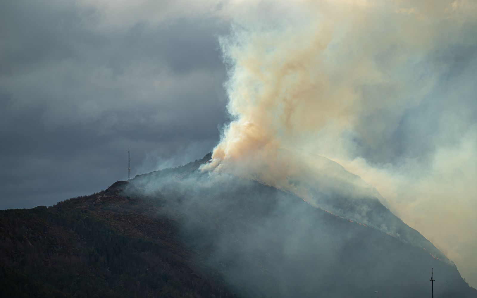 Thick smoke billowing from a forested mountainside under a hazy sky