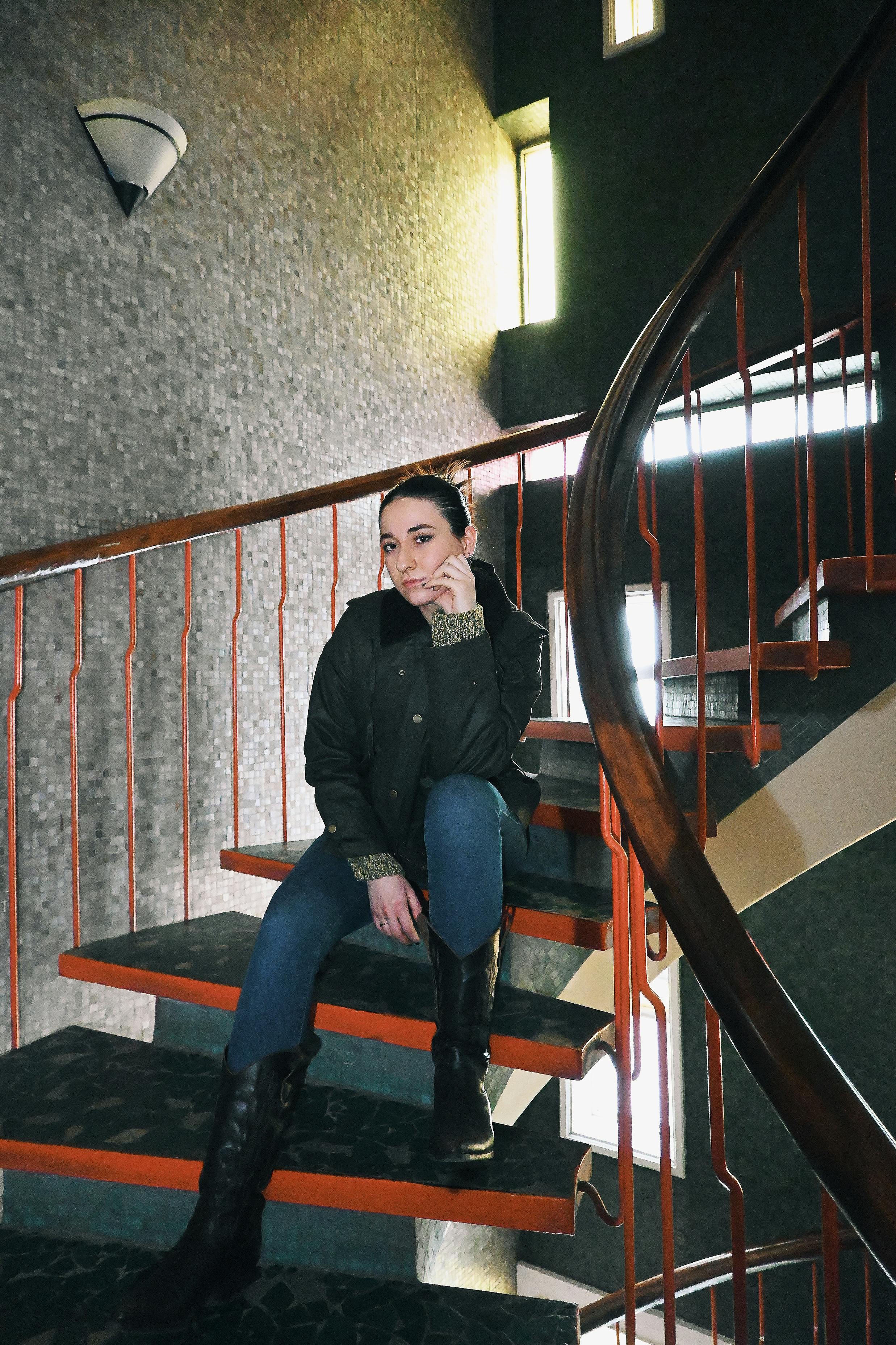 Zadarmo Sebavedomá žena sedí na modernom točitom schodisku v interiéri a vyžaruje štýl a vyrovnanosť. Fotka z fotobanky