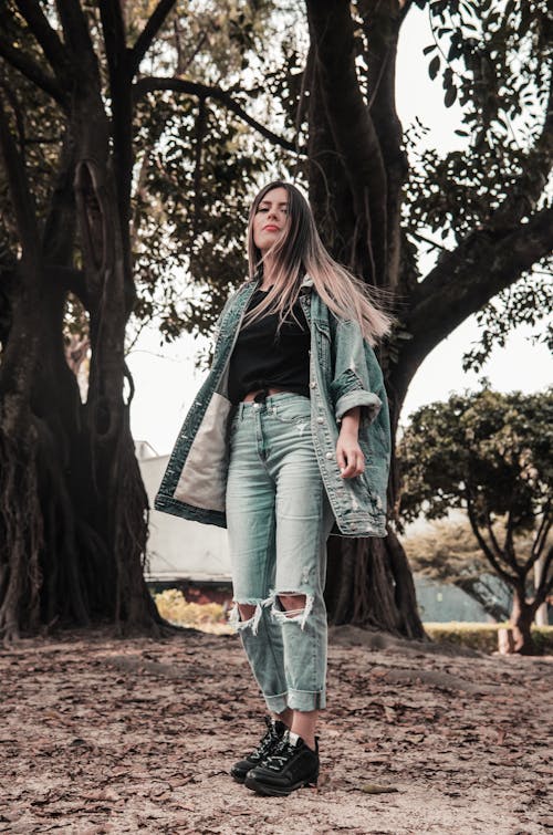 Photo of Standing Woman in Blue Denim Jacket and Jeans Posing With Trees in the Background