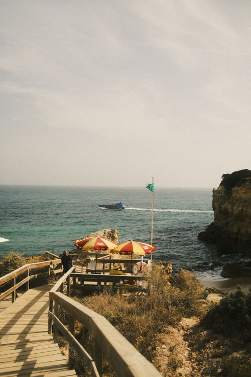 Free A picturesque beachside cafe overlooking the ocean with a boat passing by under a clear sky. Stock Photo