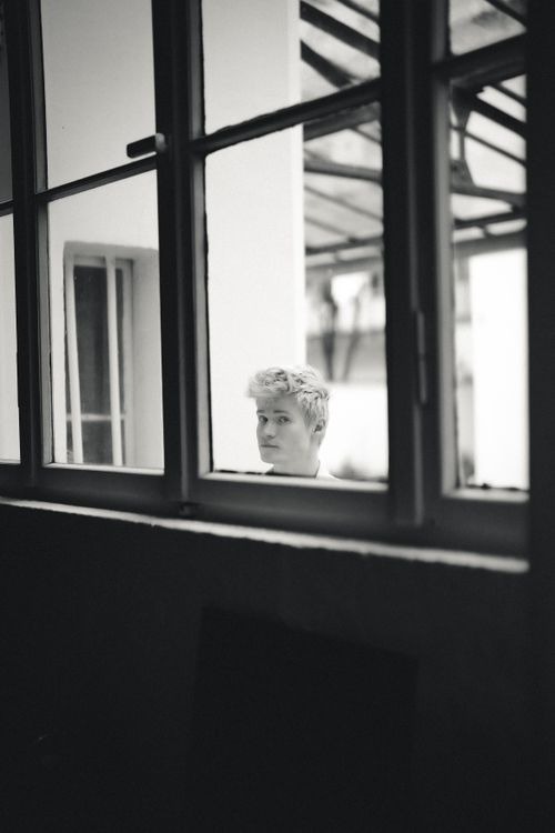 Free A black and white portrait of a person viewed through a window frame, adding a contemplative mood. Stock Photo