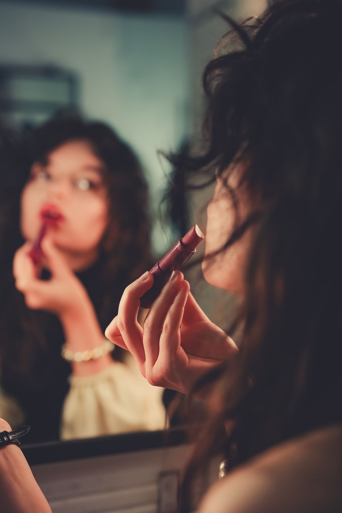 Woman applying lipstick while looking into a mirror.