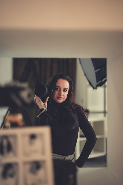 Free Portrait of a stylish woman holding a camera, creating a professional indoor studio ambiance. Stock Photo