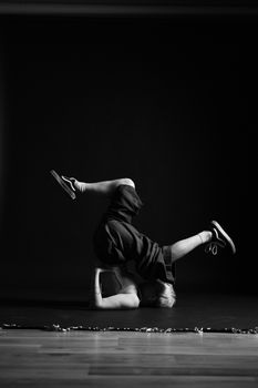 A young dancer doing a breakdance move in a dimly lit studio.